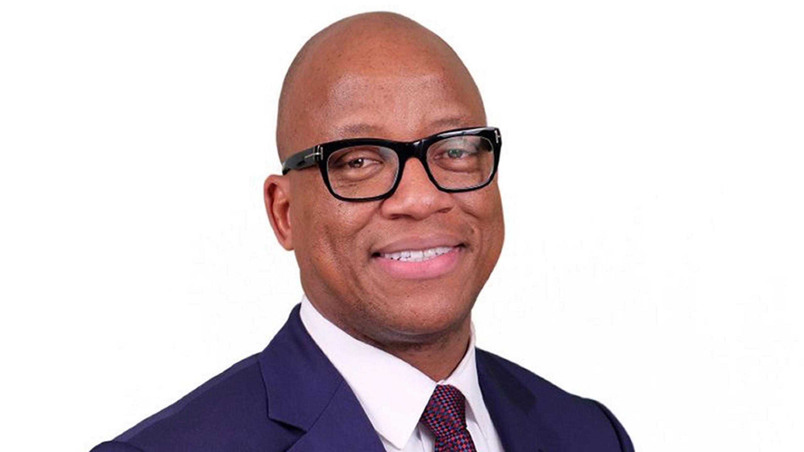 An headshot of Prof Kevin Fenton, a man wearing black-rimmed glasses, a blue suit jacket, white shirt and red tie standing against a white background