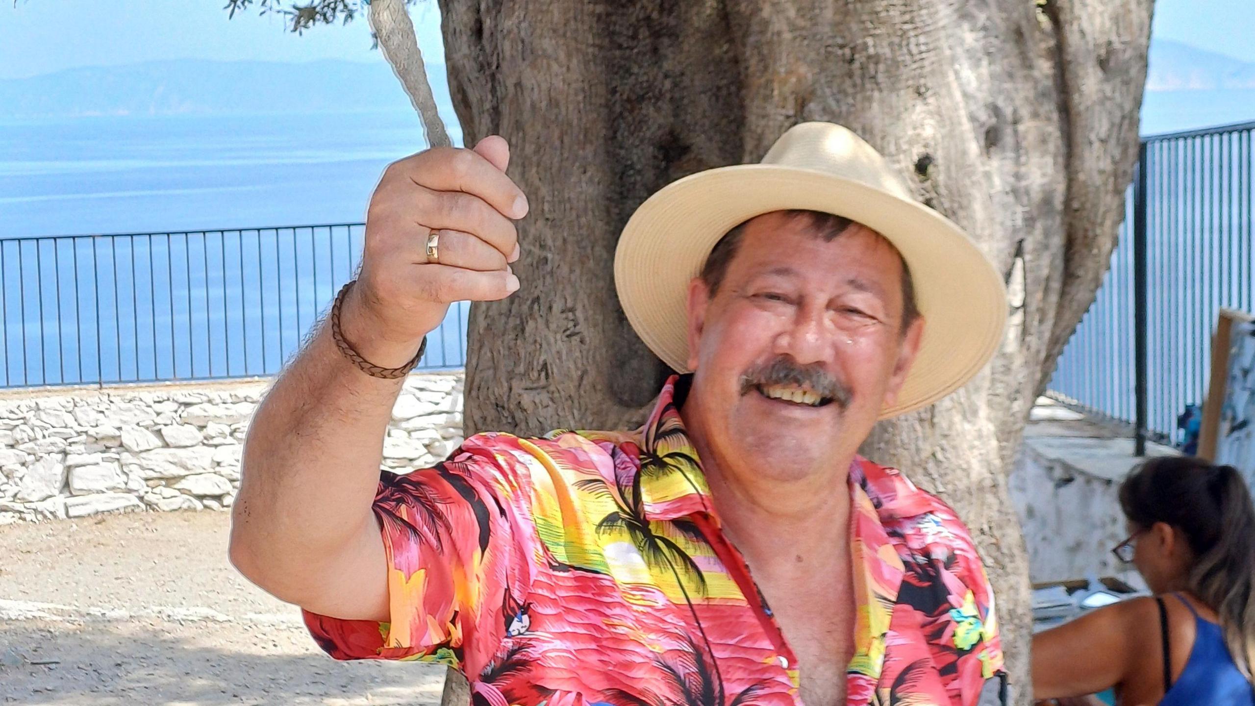 John Canning smiling with a pink Hawaiian shirt and a straw hat on