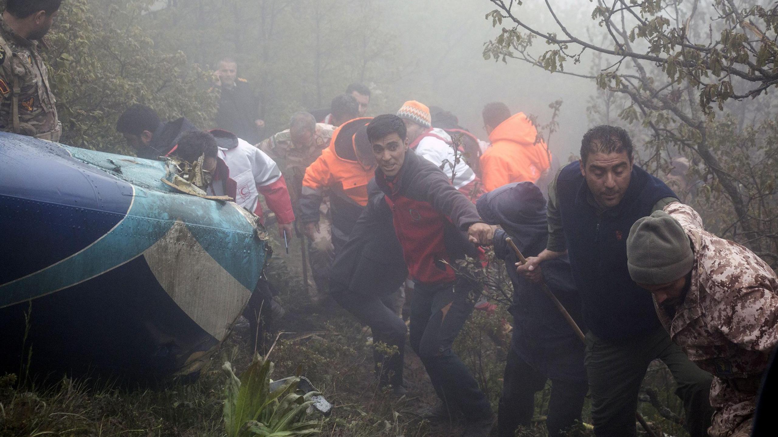 Iranian rescuers assist each other on a mountainside, next to the tail of a helictopter that crashed (20 May 2024)