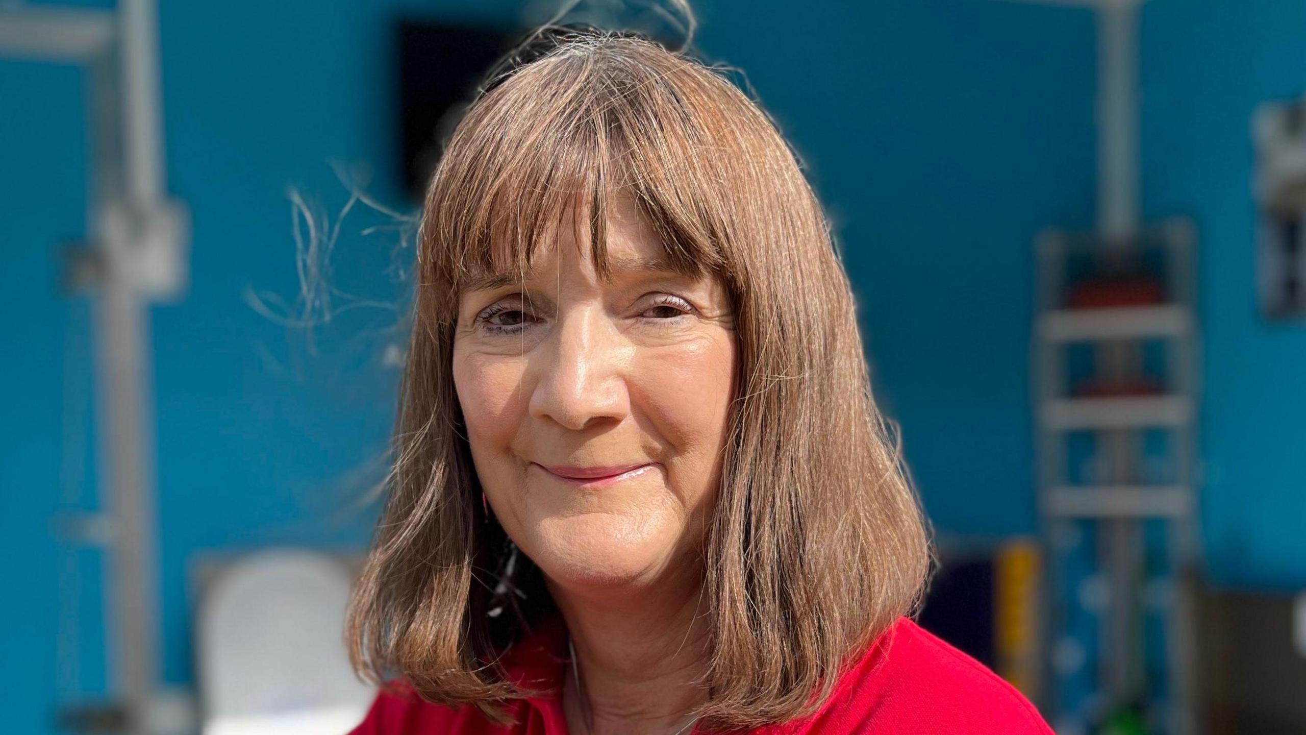 A portrait picture of Flood Mary, who is wearing a red top and is smiling at the camera.