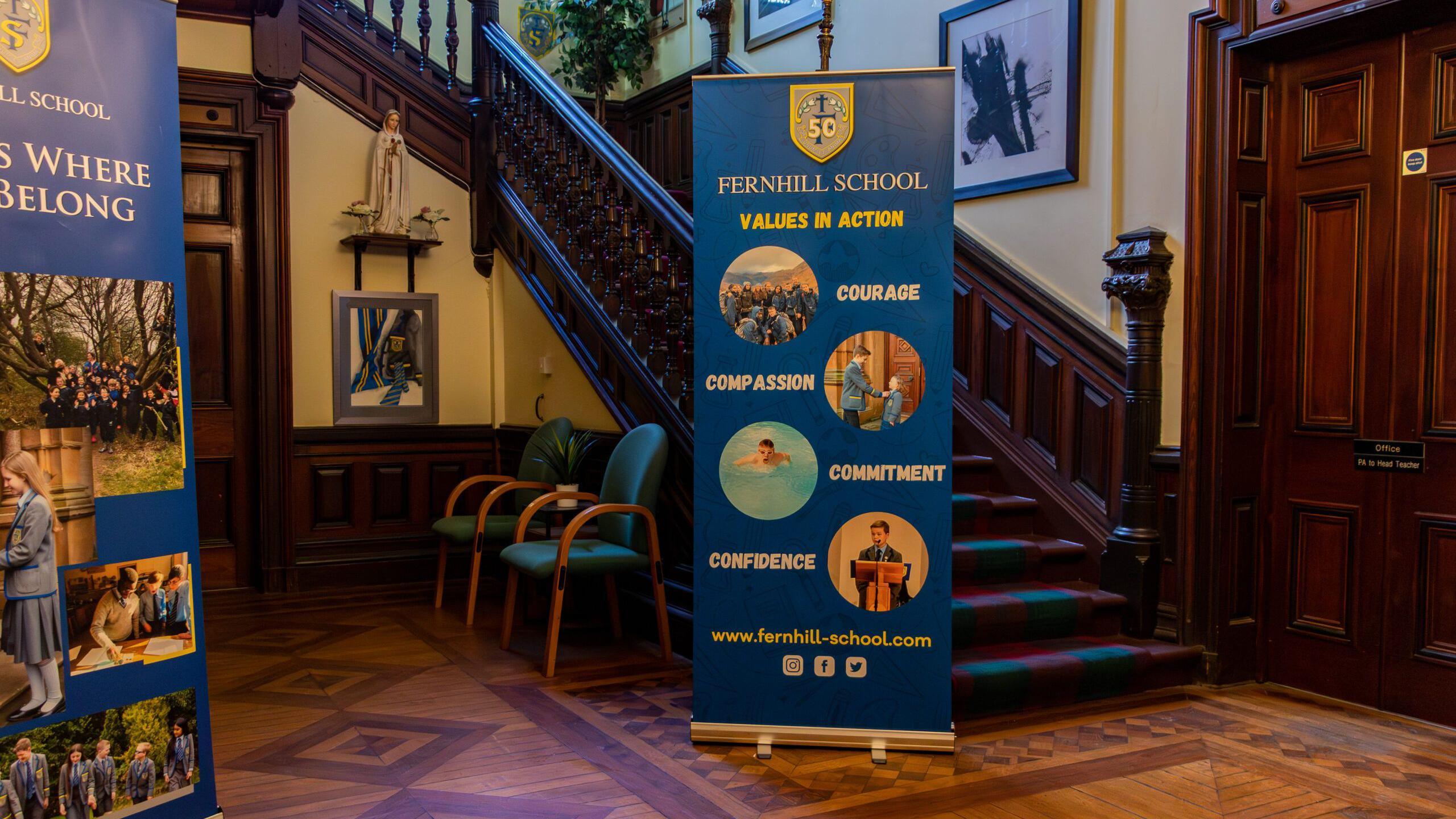 A school lobby, with wood panelled floor and a large banner saying Fernhill School - Values In Action