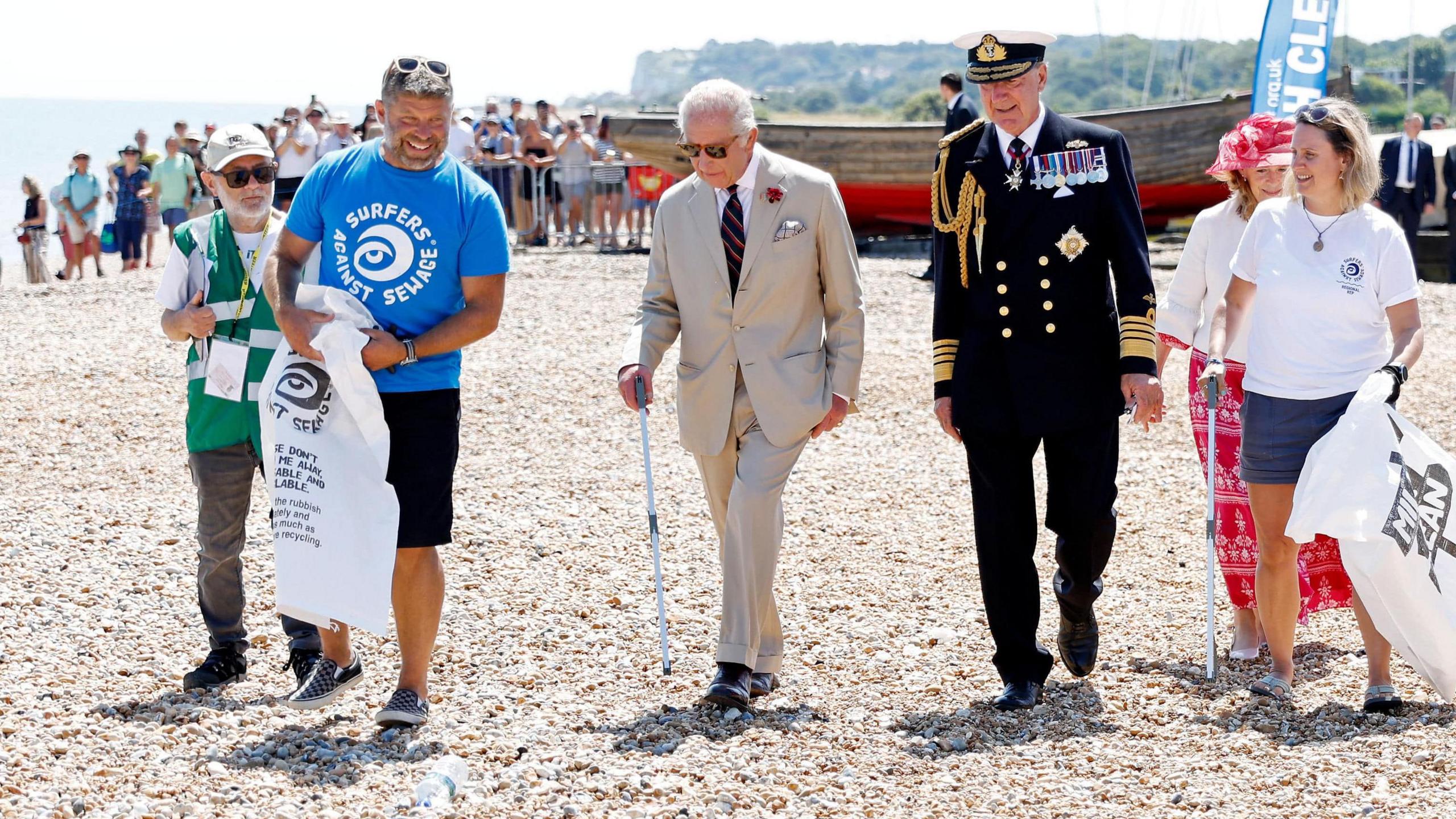 King Charles III wearing dark glasses and walking with a litter pick up stick joins a community beach clean-up initiative in Deal on the shingle beach