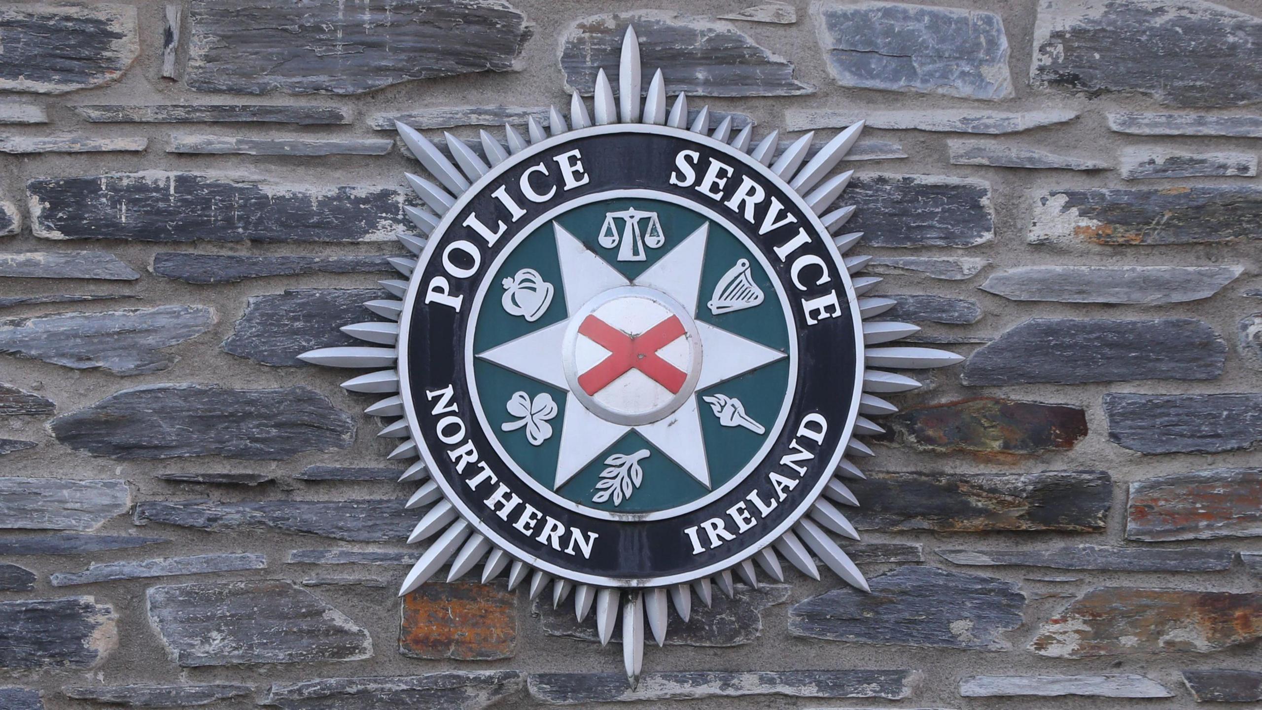 The PSNI logo on a grey brick wall. 