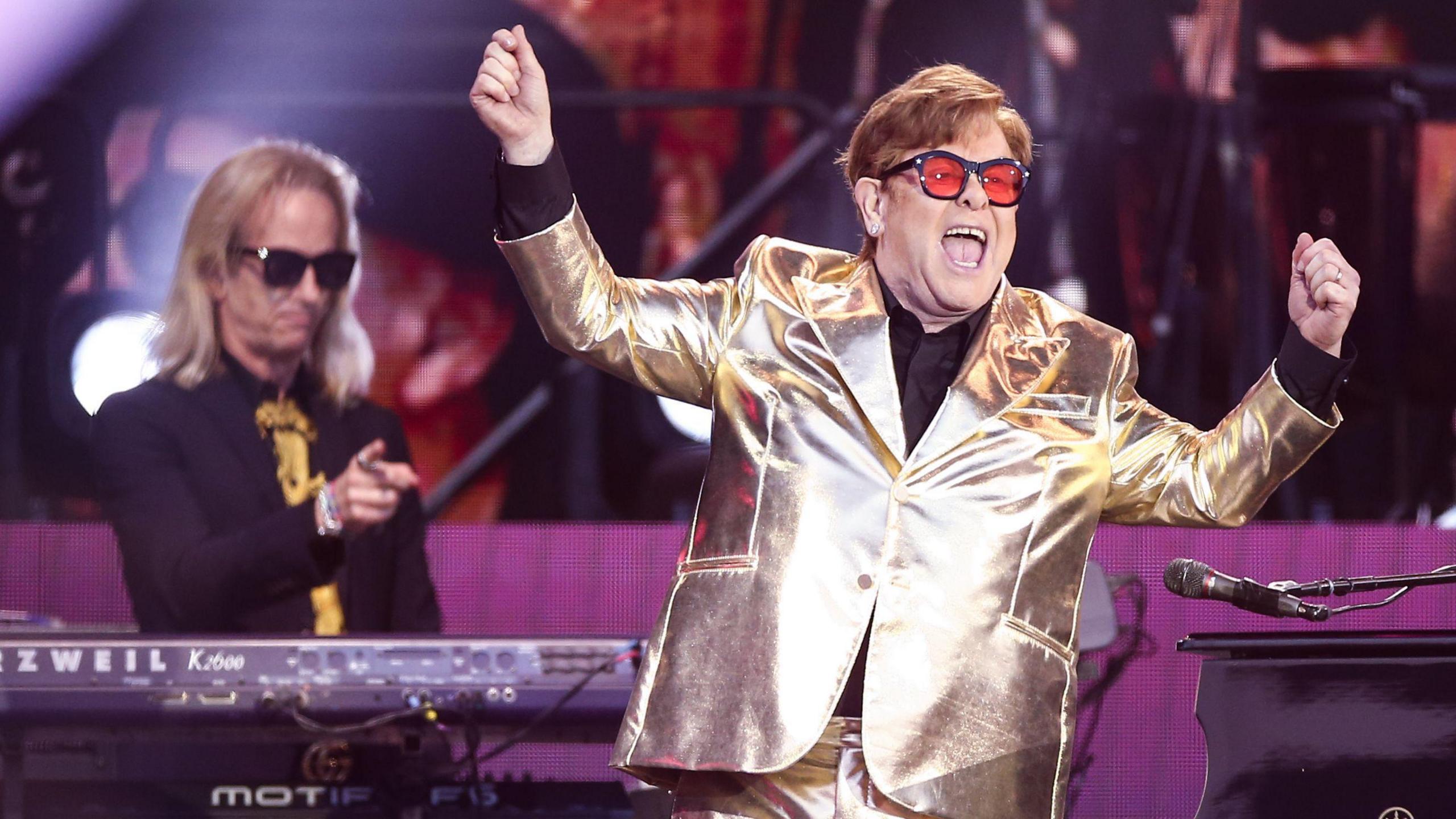 Elton John, wearing a shiny gold suit and red glasses, performs at Glastonbury Festival in June 2023.