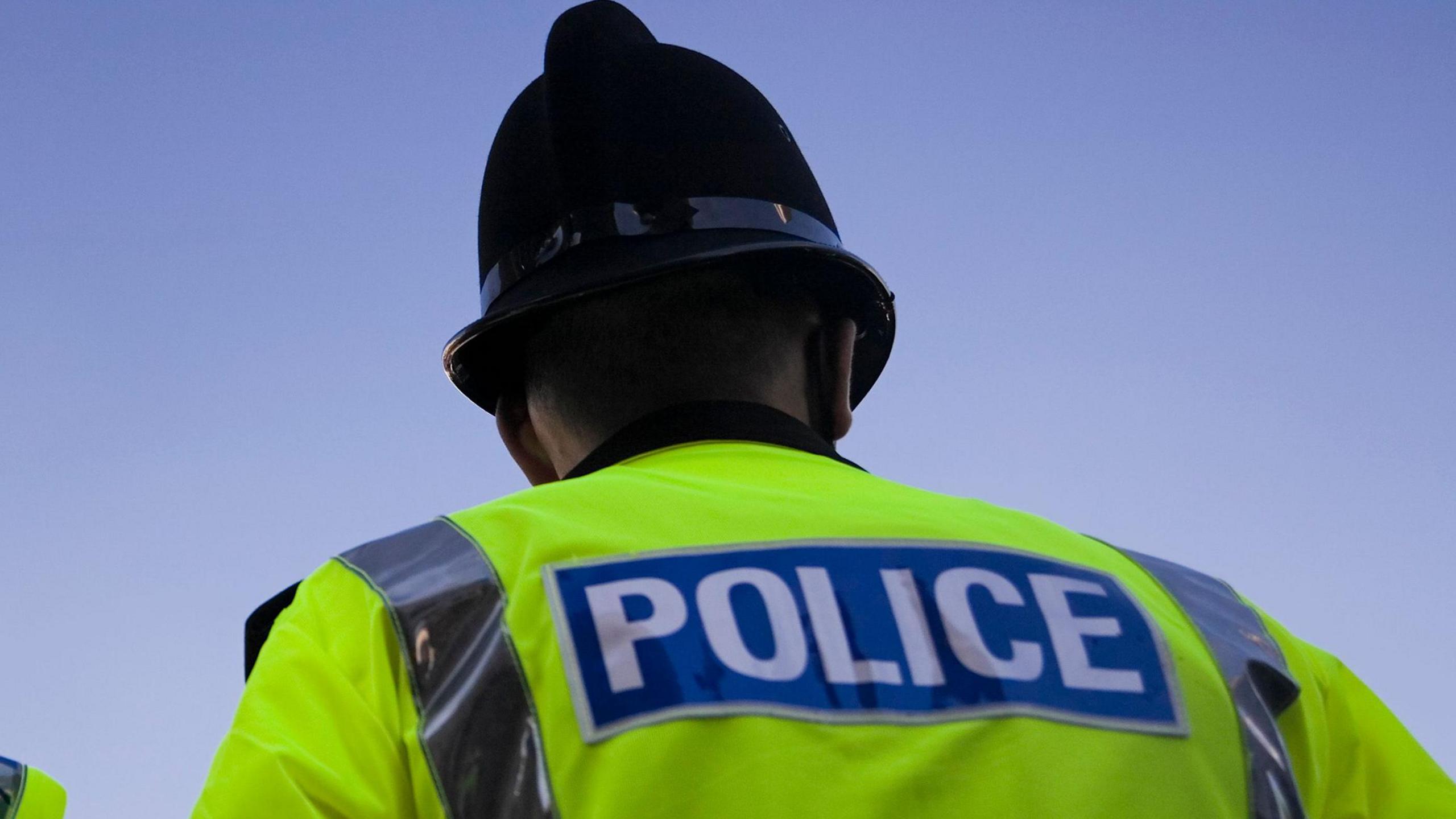 A generic image of the back of a police officer wearing a high vis a jacket and police hat 