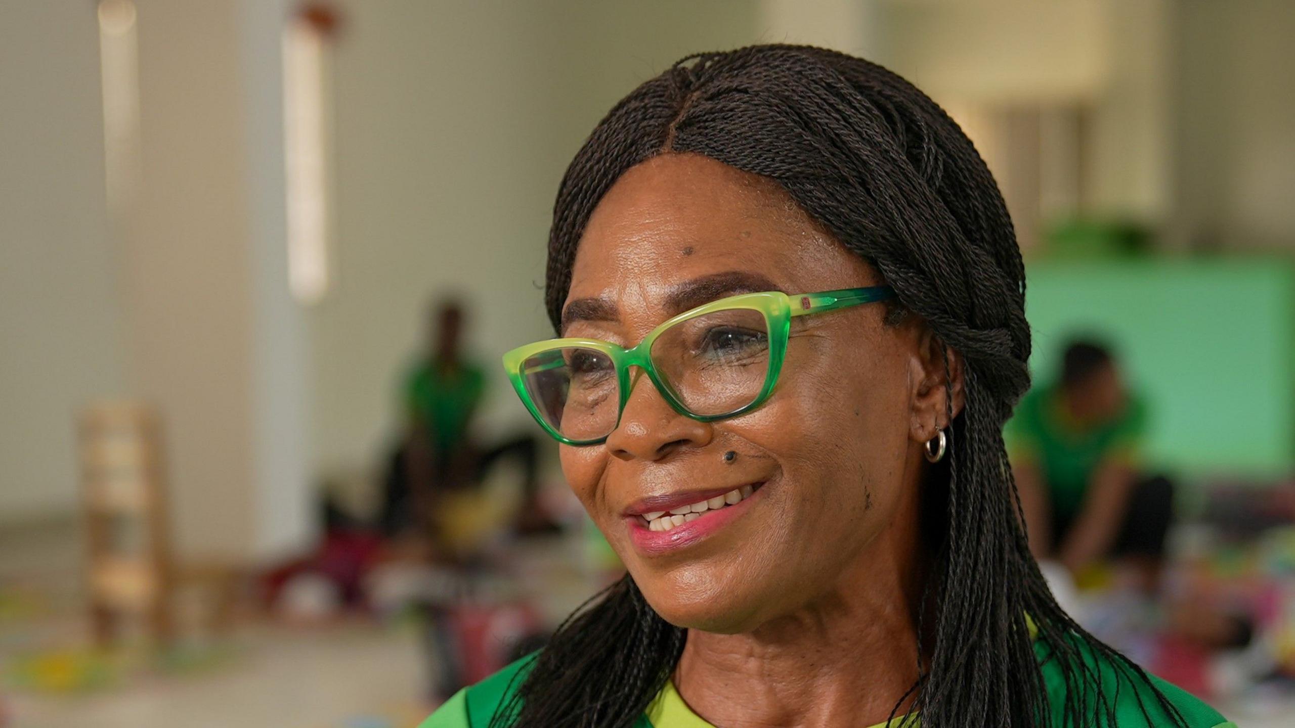 A close-up photo of Nonye Nweke wearing green glasses. She has long hair.