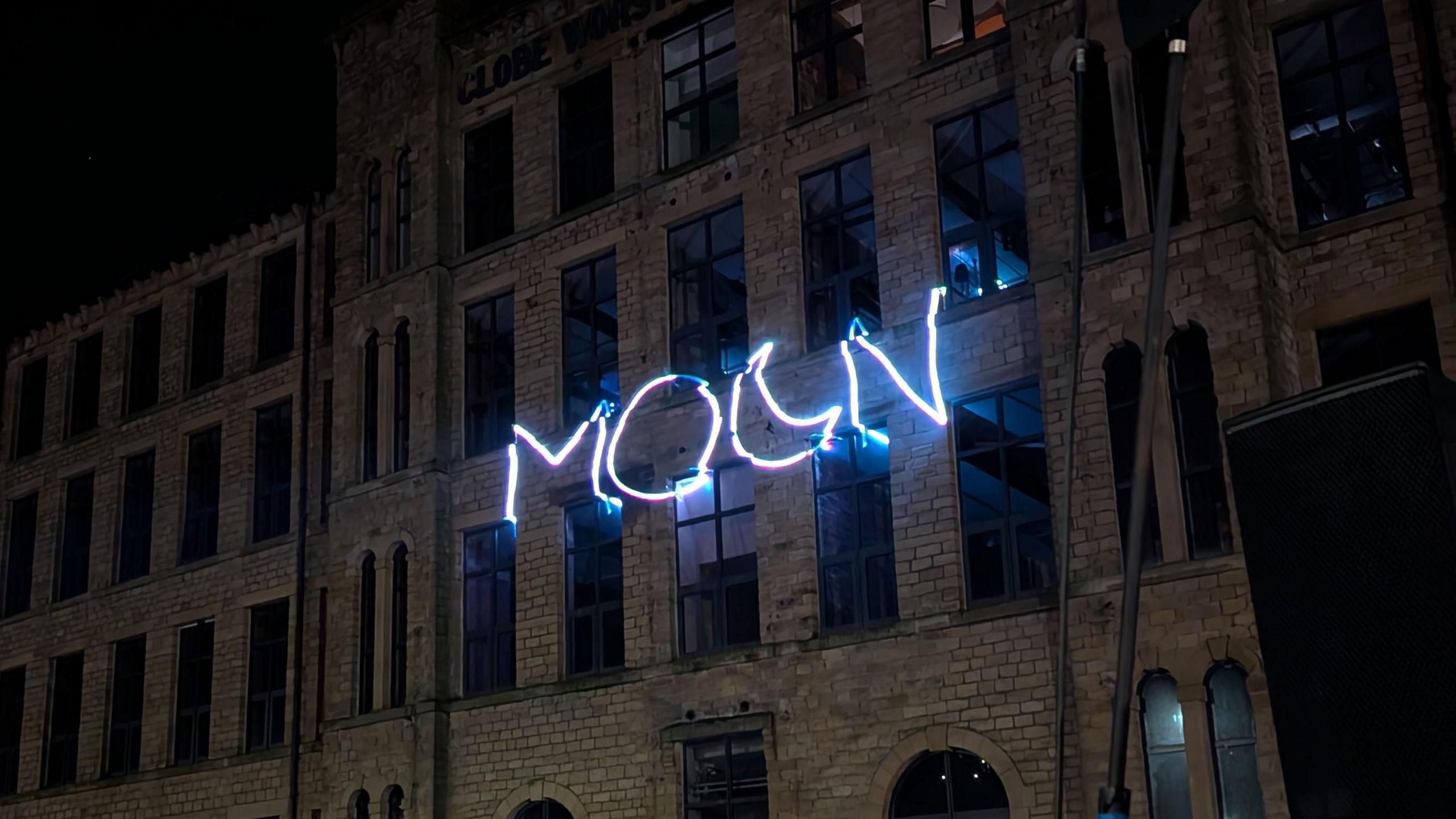 Mill buildings overlooking the canal with the word 'Moon' projected on to them