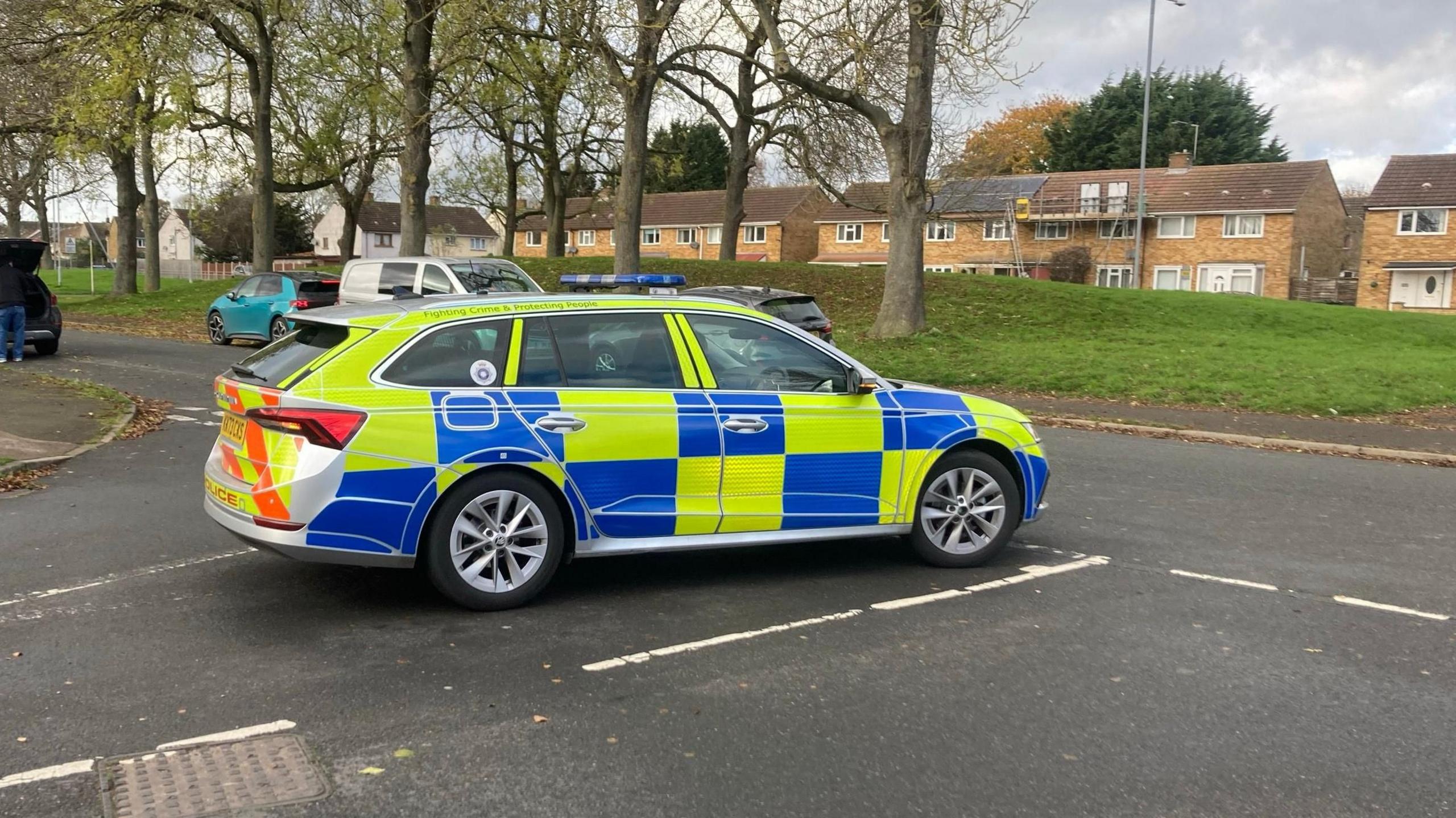 A police car is stationary on a road. Trees and houses can be seen in the background
