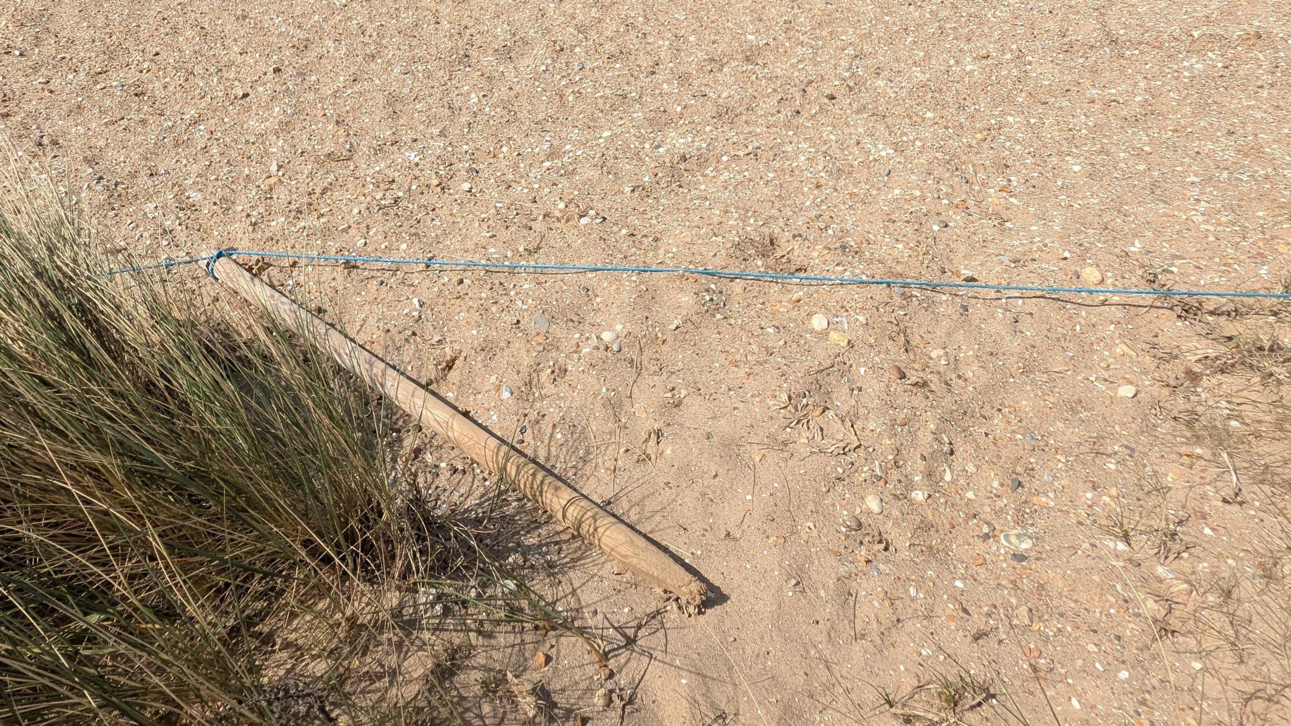 A post with blue rope attached which has been pulled out of the ground and is laying on the sand.