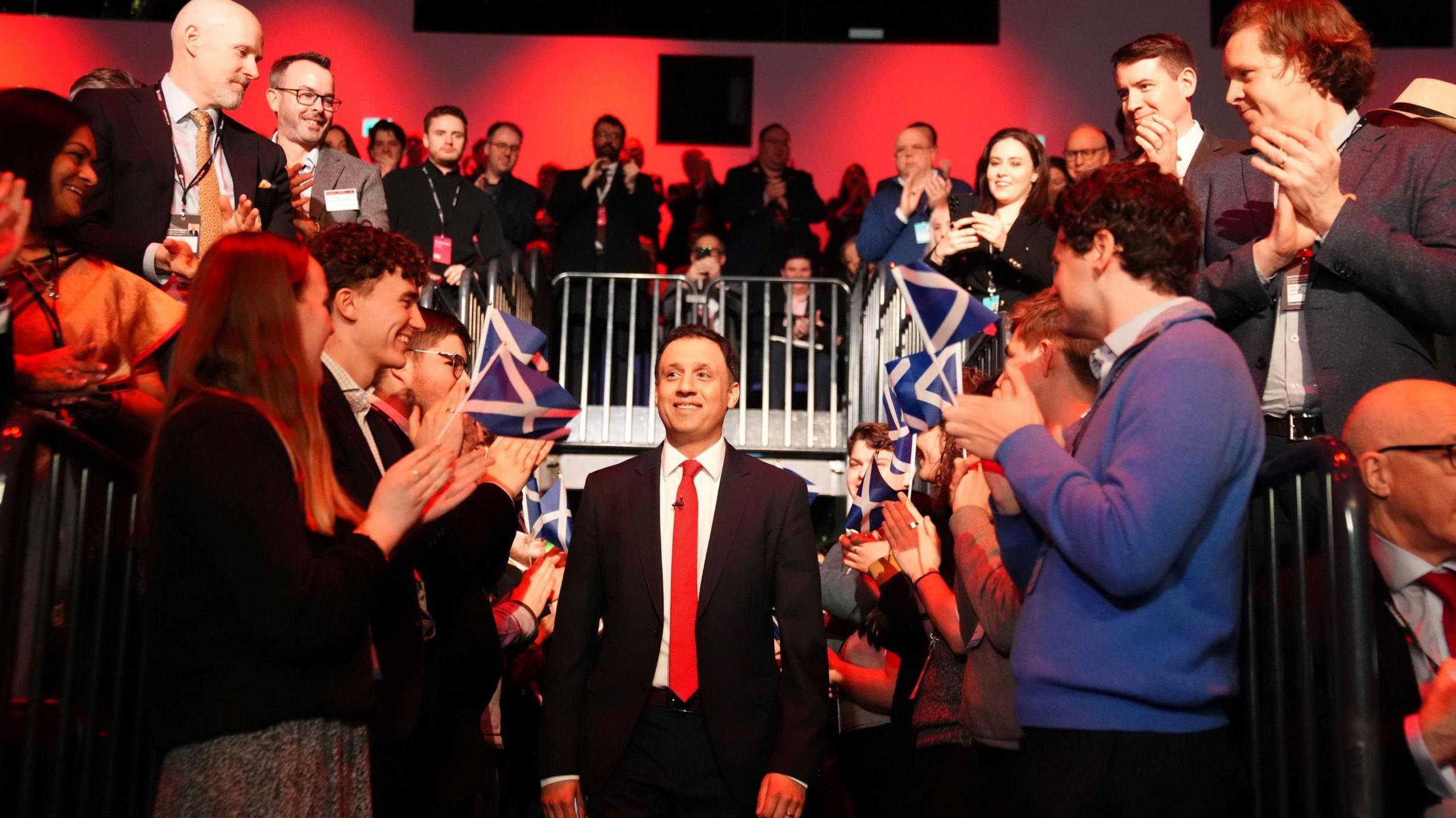 Anas Sarwar walks out at the Labur conference. Cheering supporters surround him on either side, waving flags