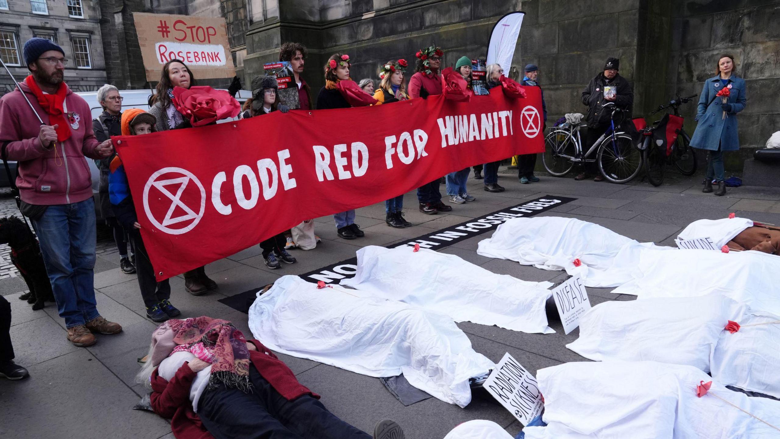 Protesters at the Court of Session in Edinburgh. Some are holding a big banner saying CODE RED FOR HUMANITY while several others are lying on the ground with white sheets over them, as if they are corpses (presumably killed by the climate crisis).