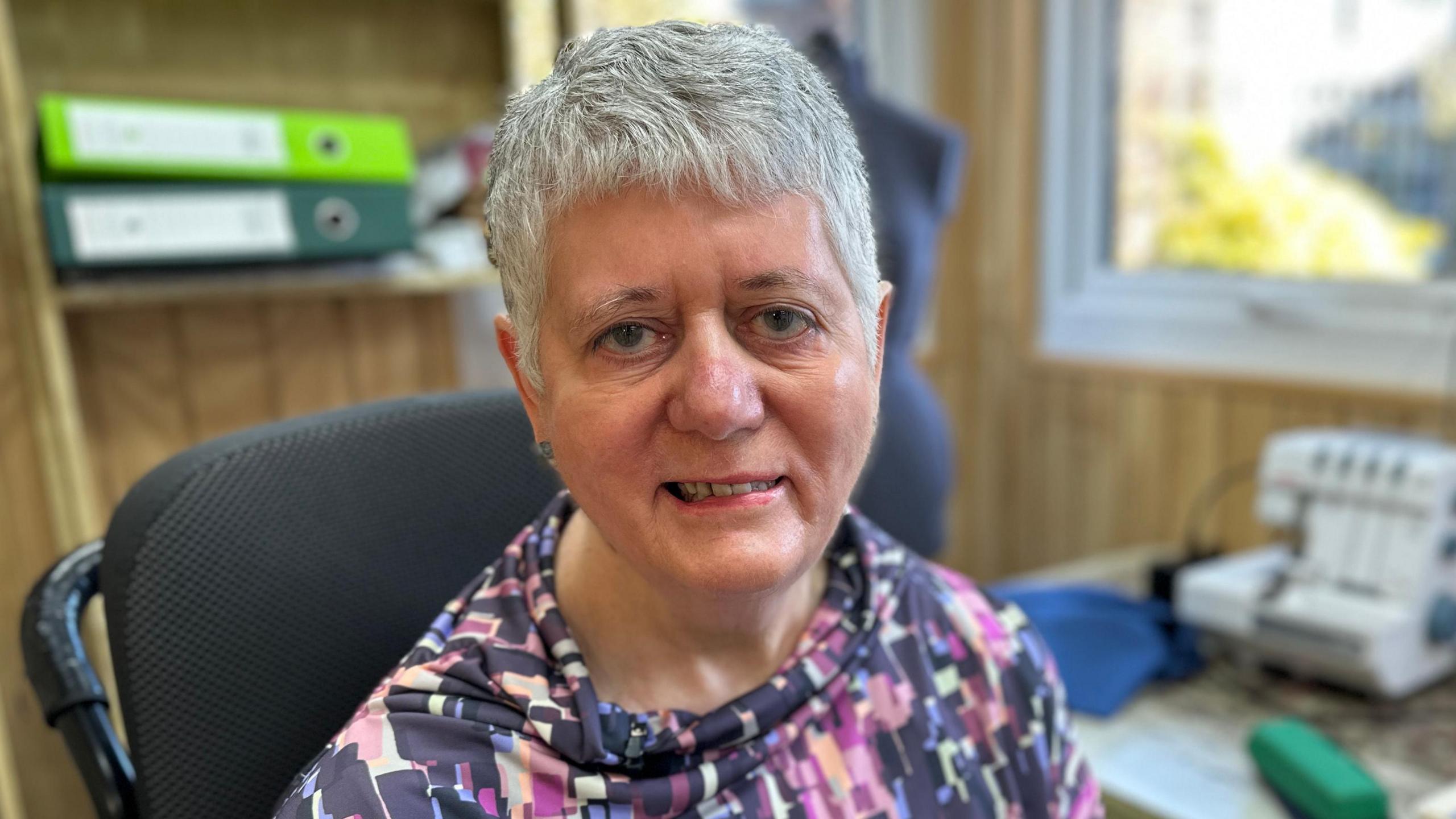 Sheila Hawkins looking at the camera. She has short grey hair and is wearing a patterned top