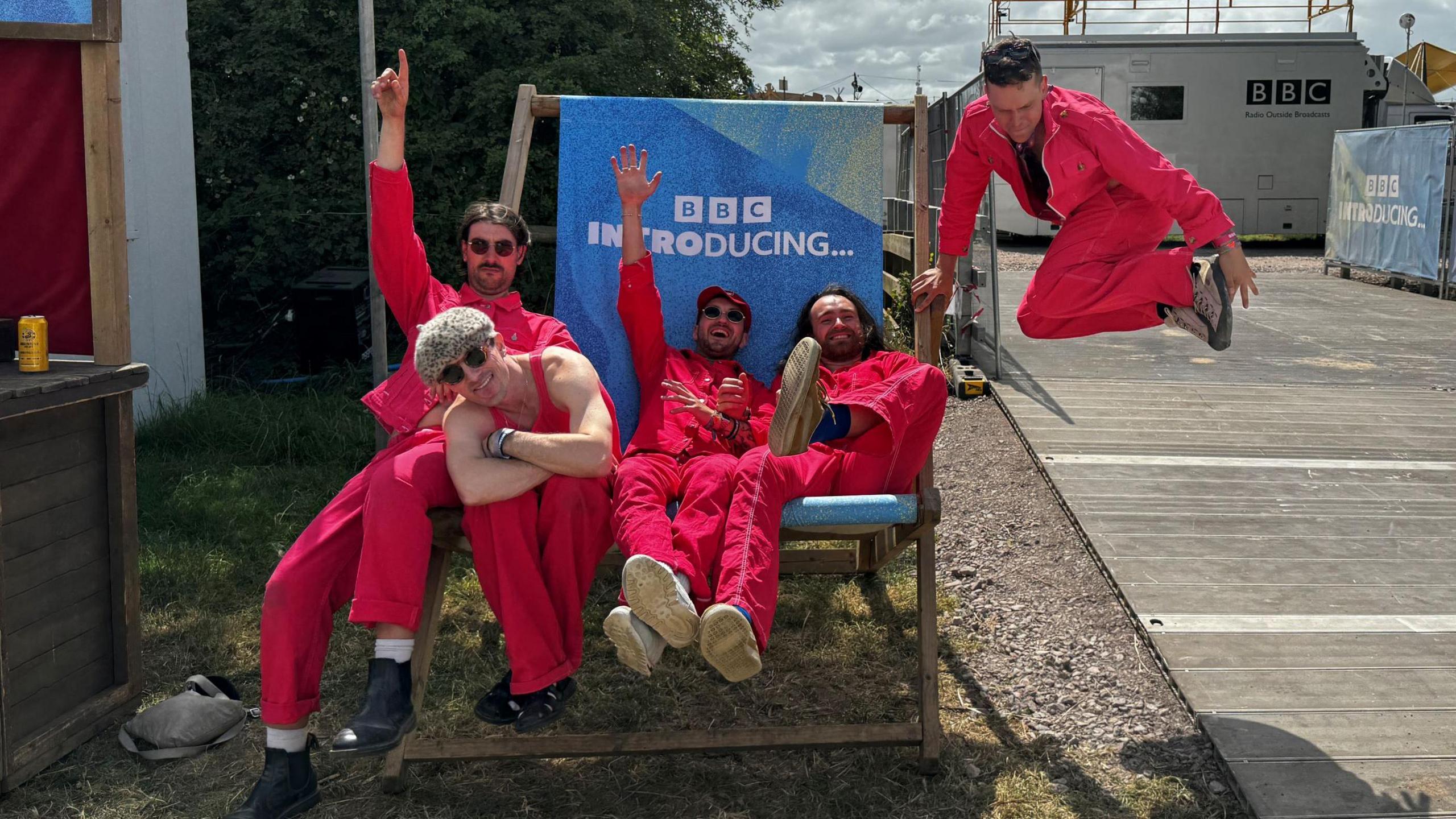 Cousin Kula wearing pink and sitting in a BBC Introducing deck chair - one member is jumping in the air next to them