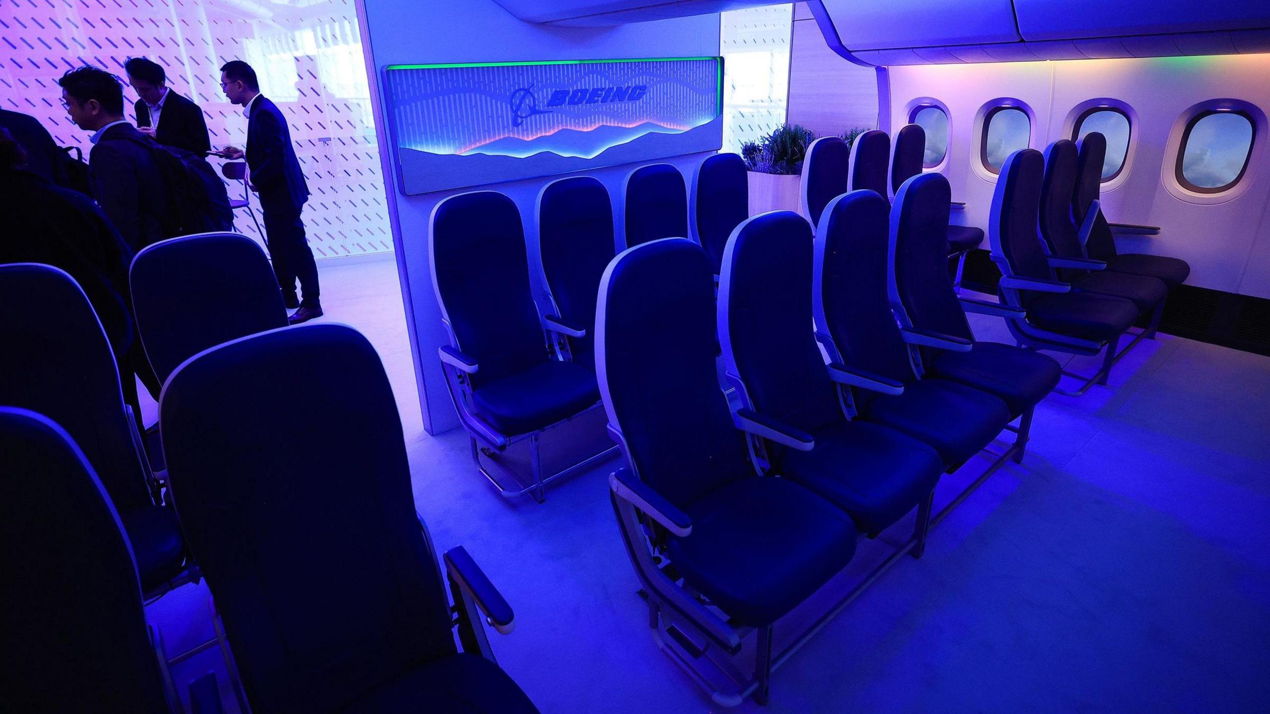 A mock-up of a 777x interior at a trade show. Seats are individually spaced, rather than joined up, with blue lighting and the Boeing logo.