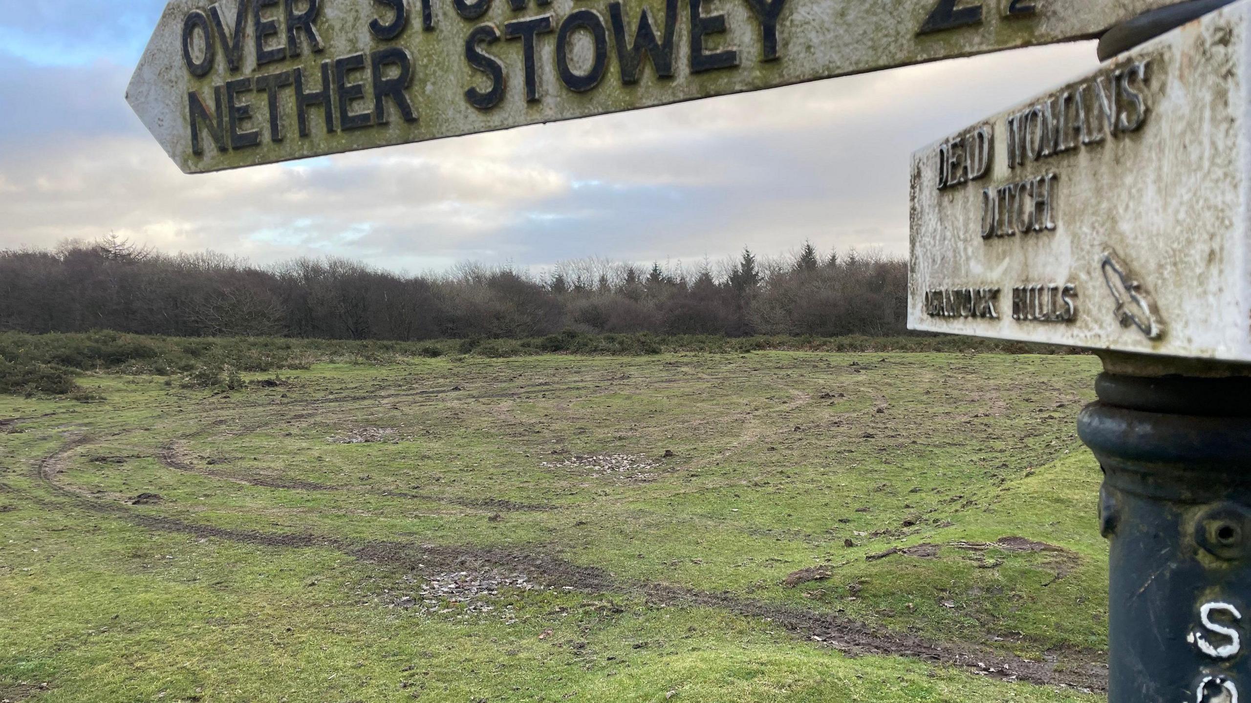 Tyre marked grassland with Dead Womans Ditch fingerpost sign 