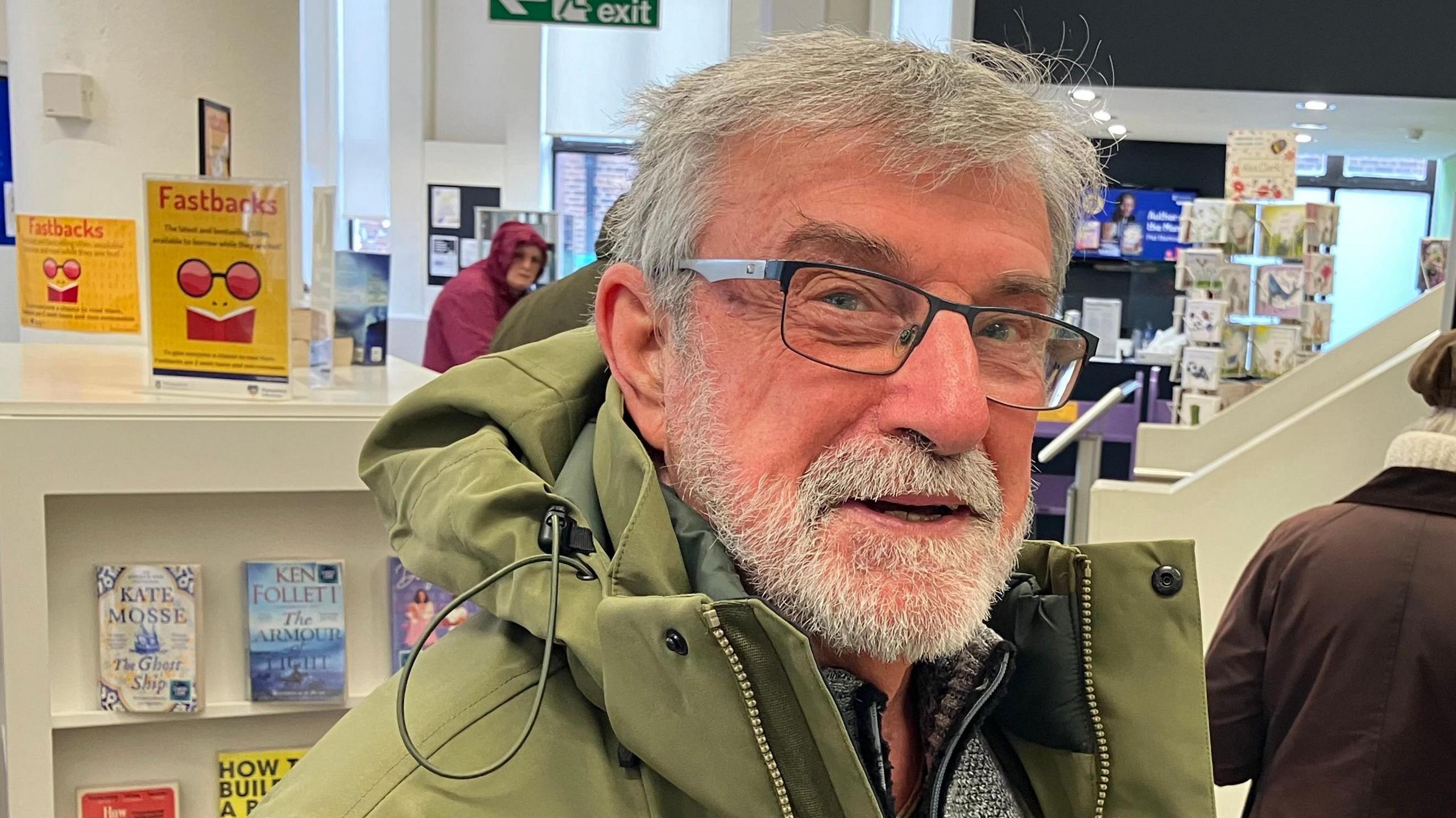 A white haired man with a beard and glasses in front of books in Gosport Discovery centre