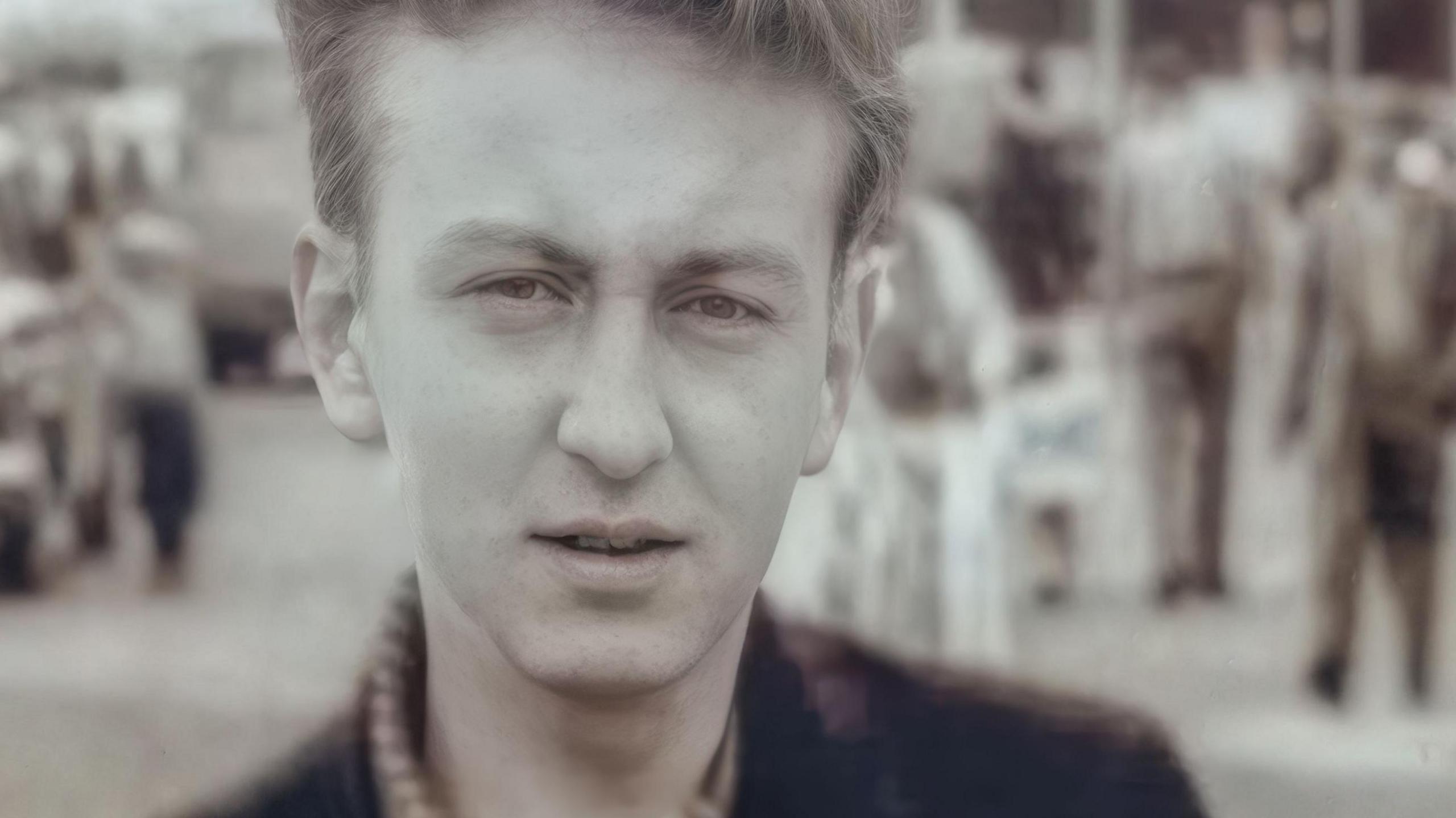 A black and white photograph of a young Fred Done, with short wavy hair and wearing a checked shirt and dark jacket