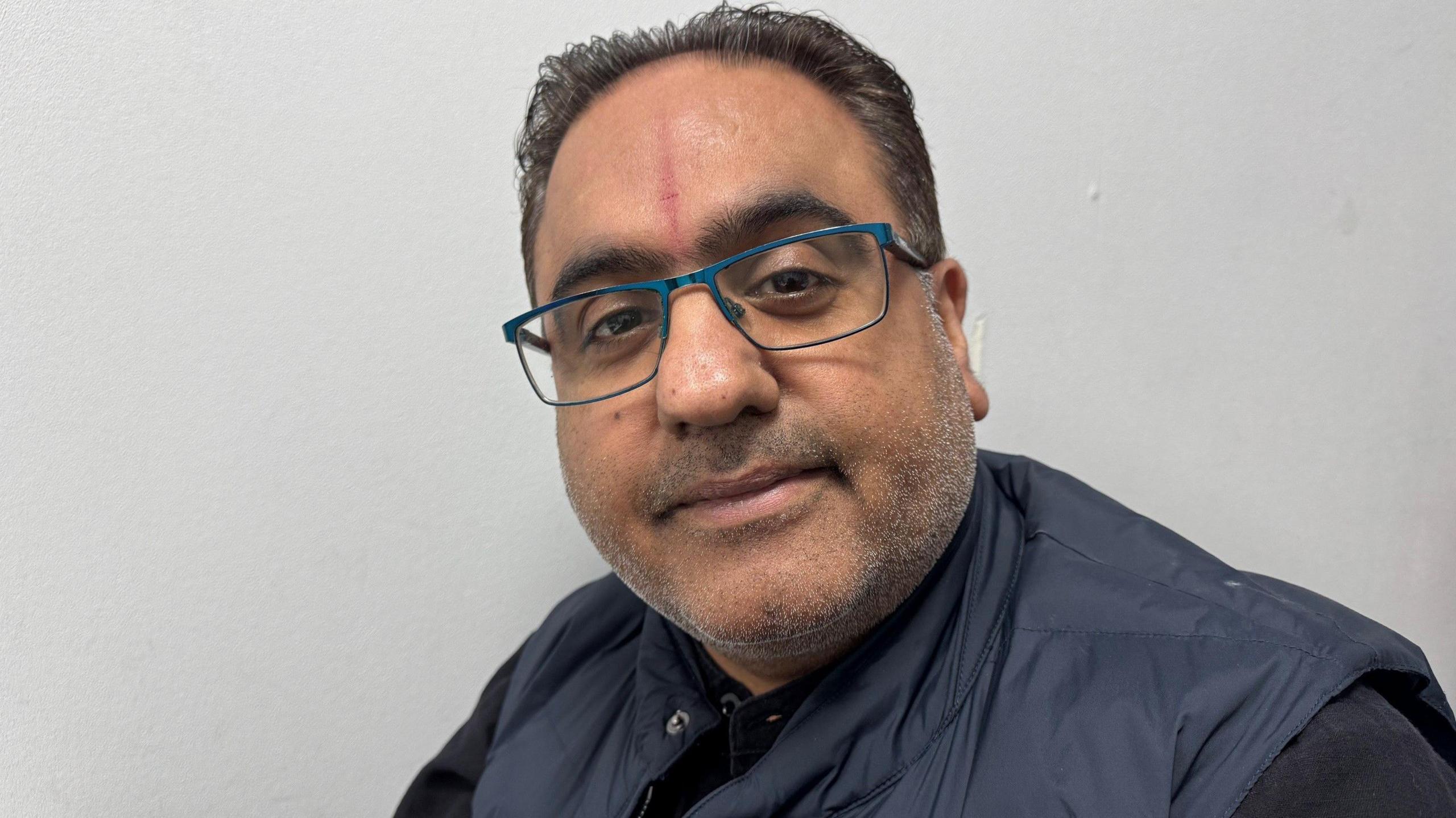 A man with glasses looks into the camera.