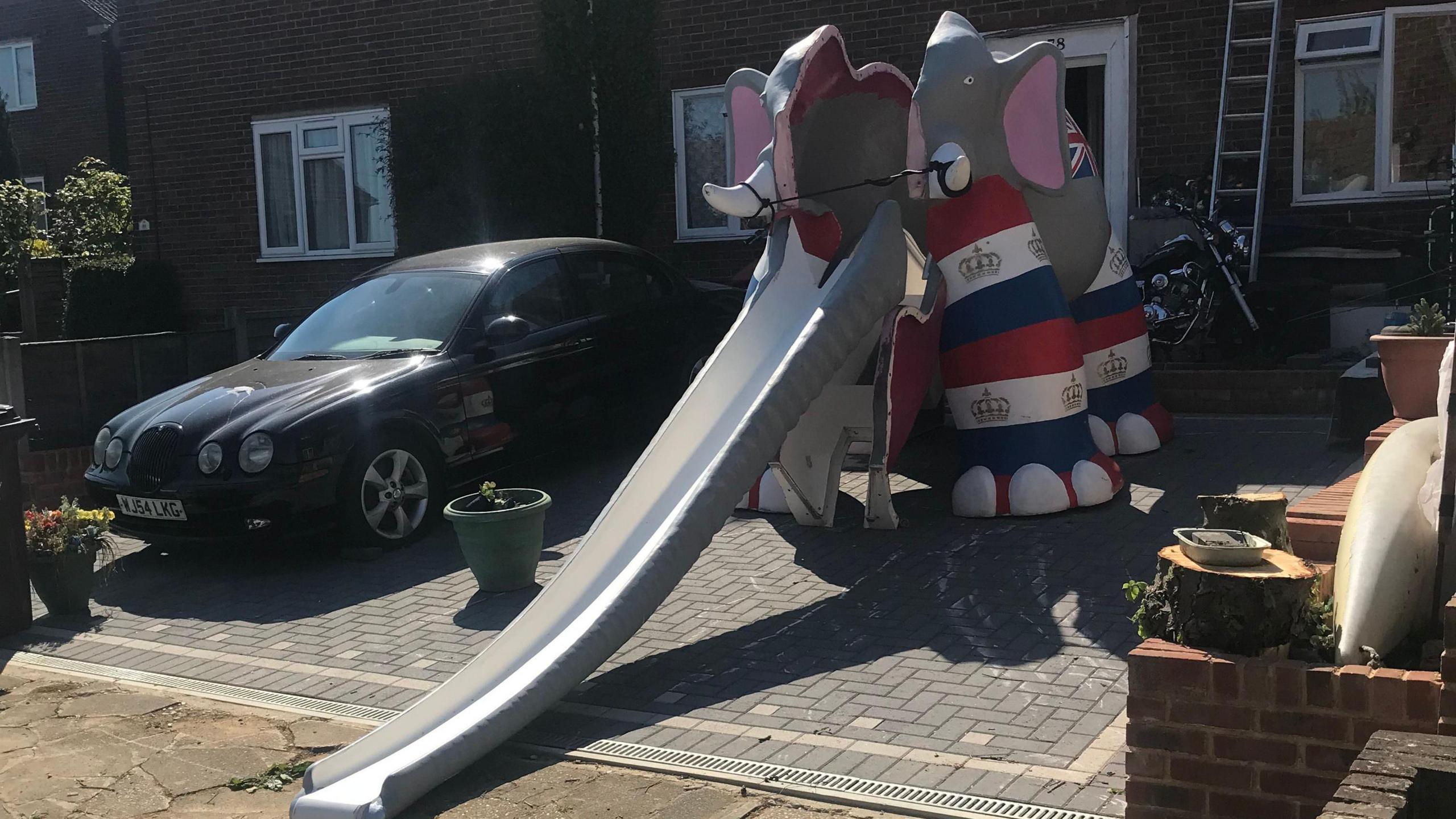 A multi-coloured elephant slide in a driveway of someone's house.