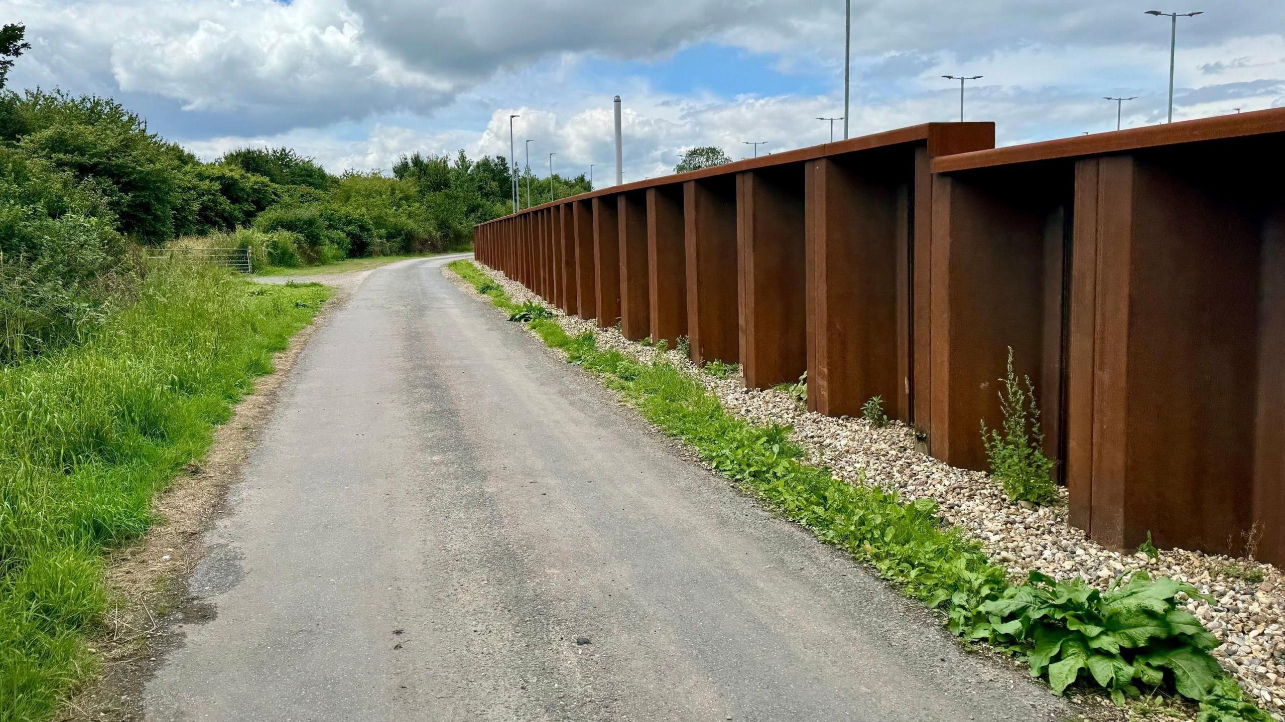 A road running through the countryside with a tall brown steel wall on the right side