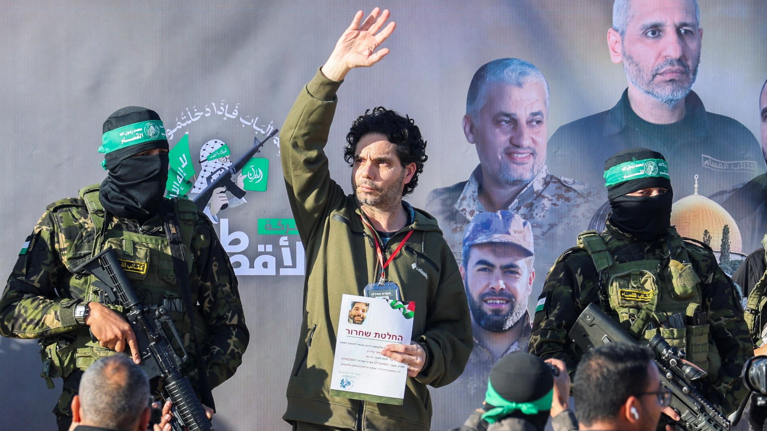 Ofer Kalderon, a hostage held in Gaza, waves from a stage in Khan Younis while flanked by two armed and masked Hamas fighters.