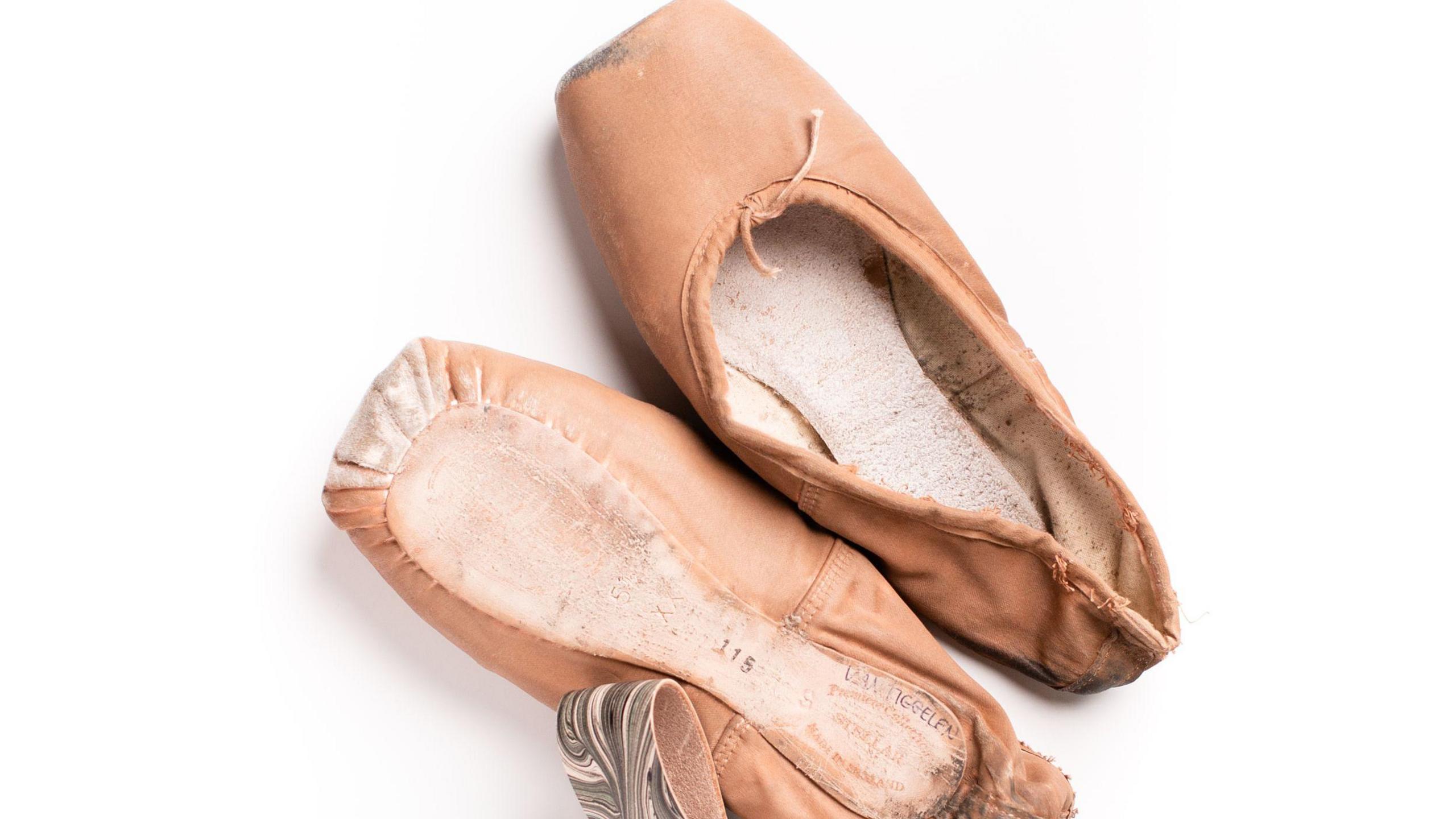 A pink pair of worn ballet shoes is placed next to a keyring and cable tidy that are decorated with a swirling marbled pattern. In grey and pink.