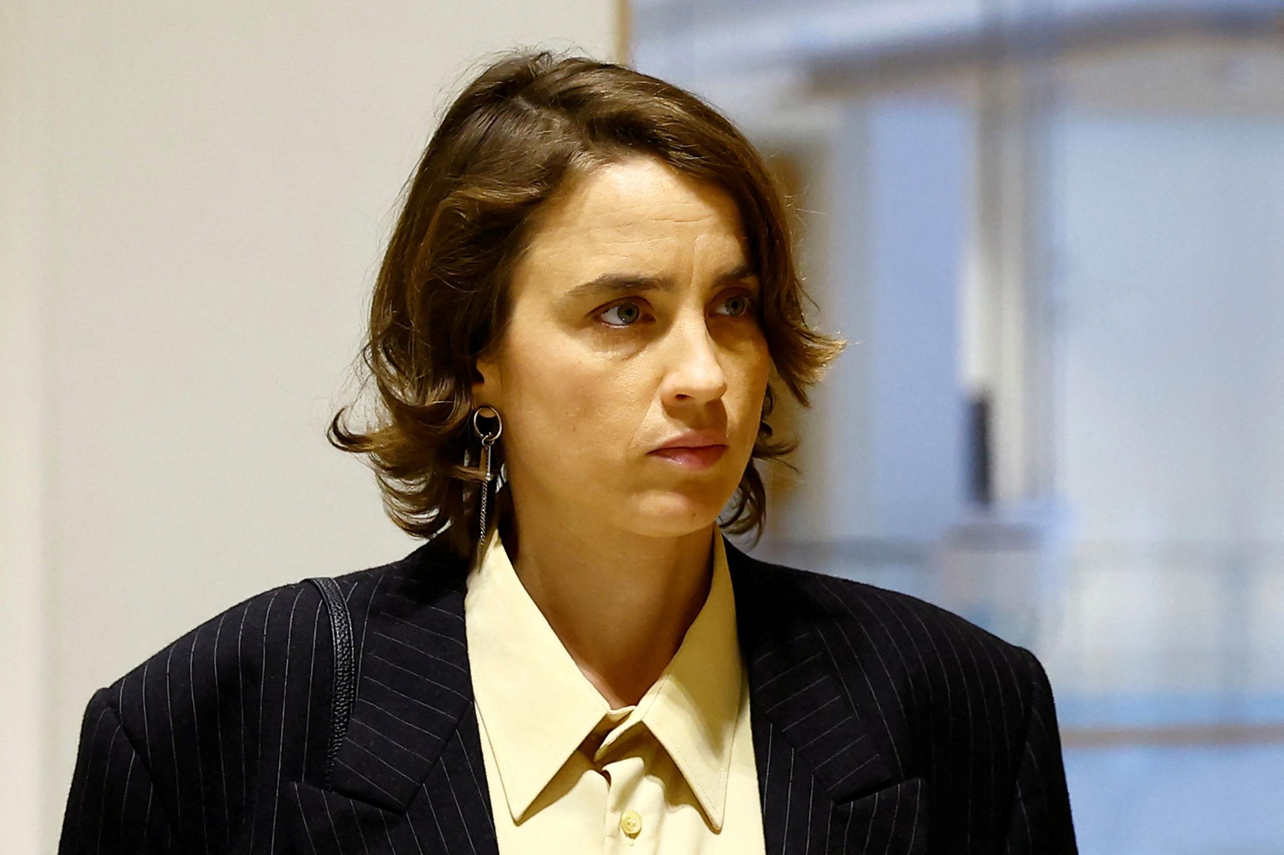 A headshot of Adele Haenel. She has short brown hair and wears a black suit jacket and yellow shirt.