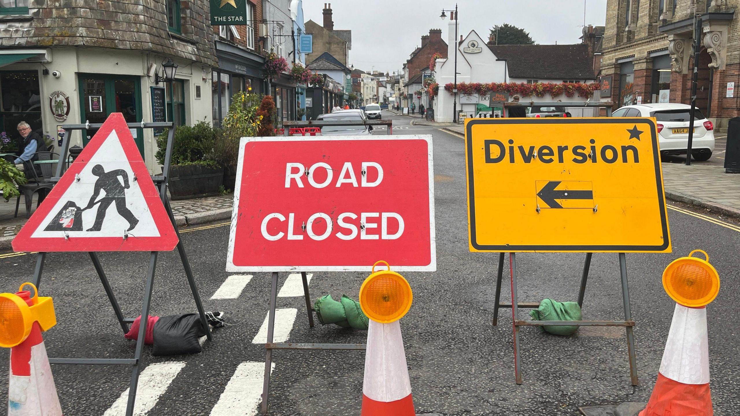 A road closed and diversion sign with buildings seen in the background