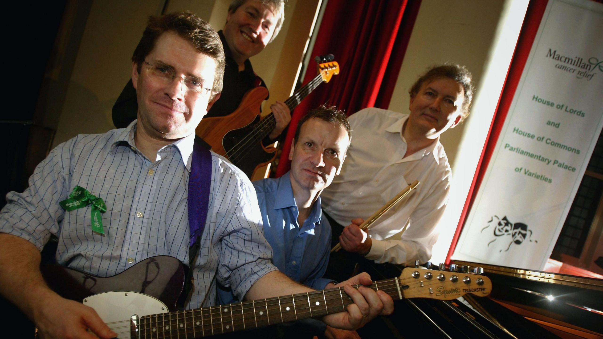 Kevin Brennan holding an electric guitar alongside three other MP musicians