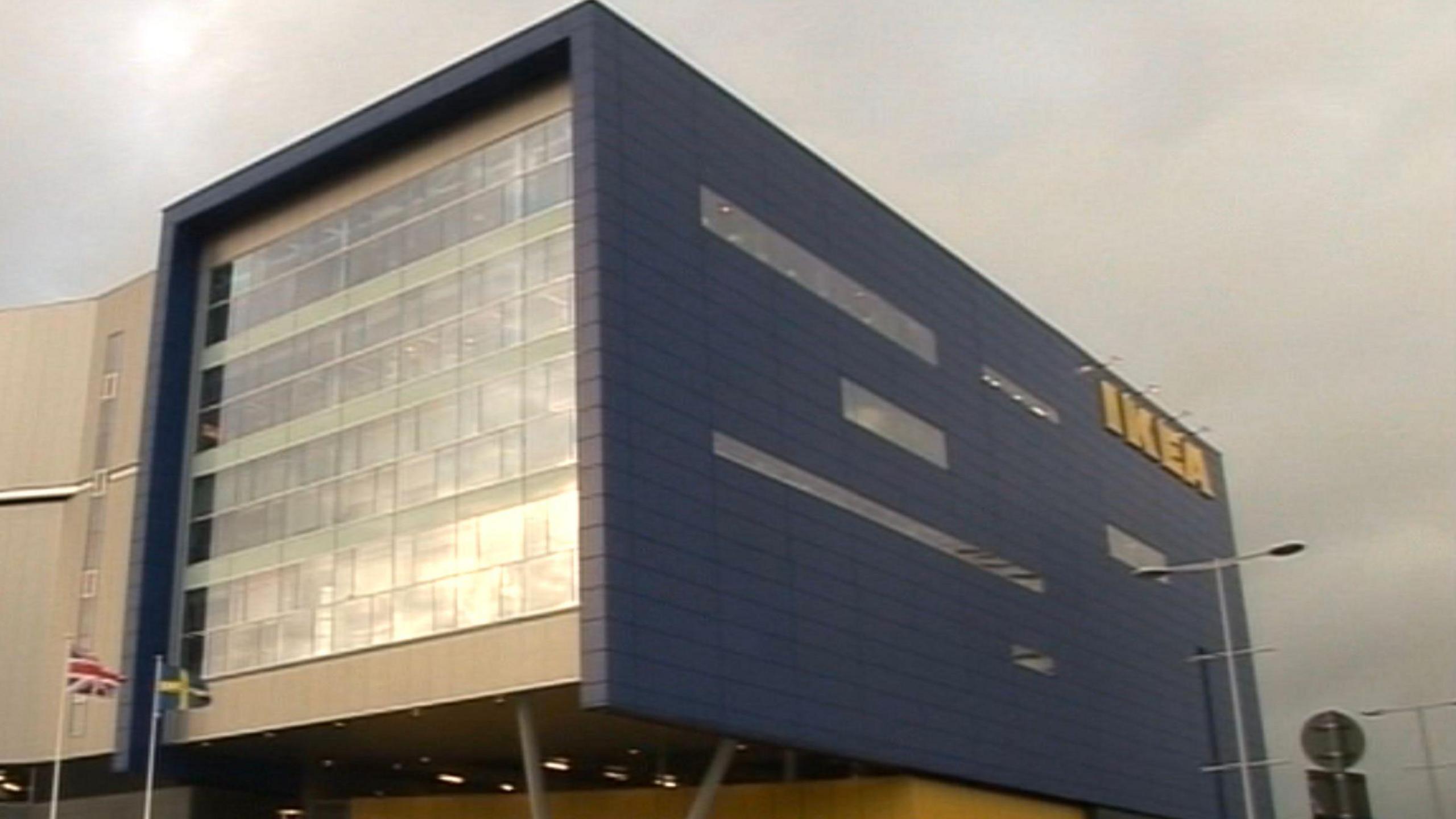 A blue and grey clad building with a yellow sign that says Ikea in the upper right side, the left of the building is covered in glass