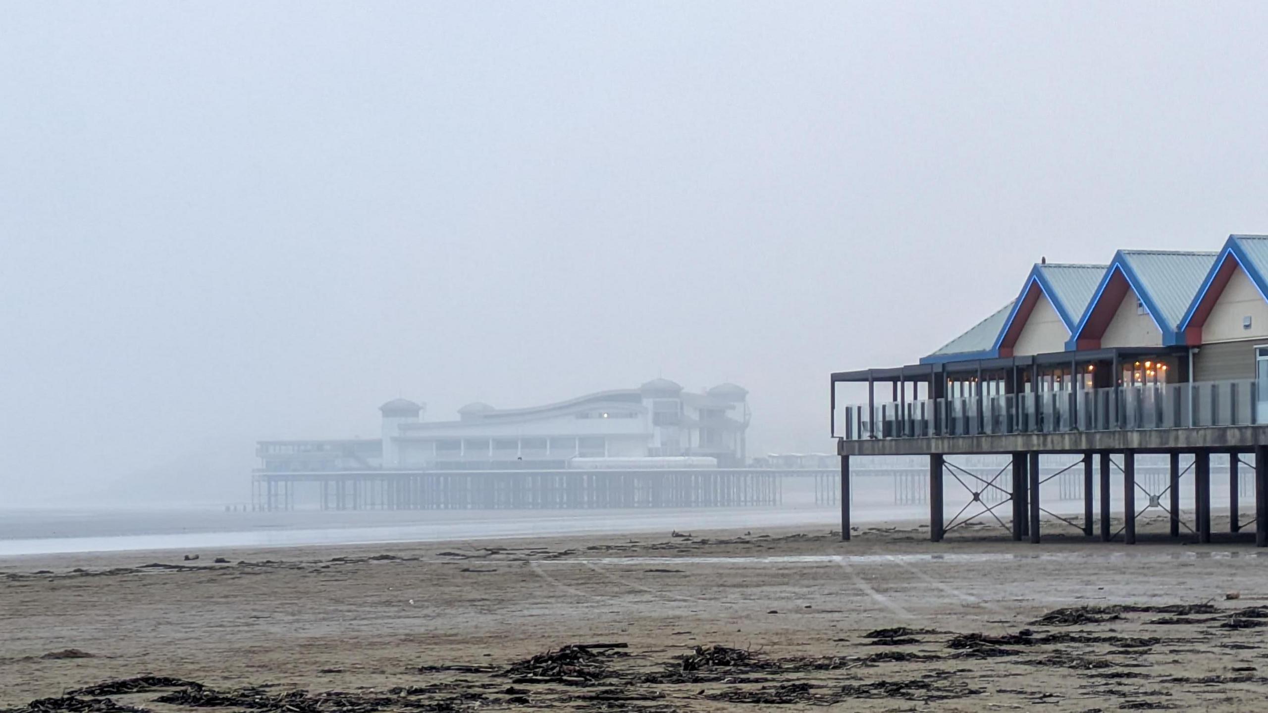 Weston-super-Mare's pier is disappearing behind fog. The beach is clear in the foreground but fog is rising above the water in the background.