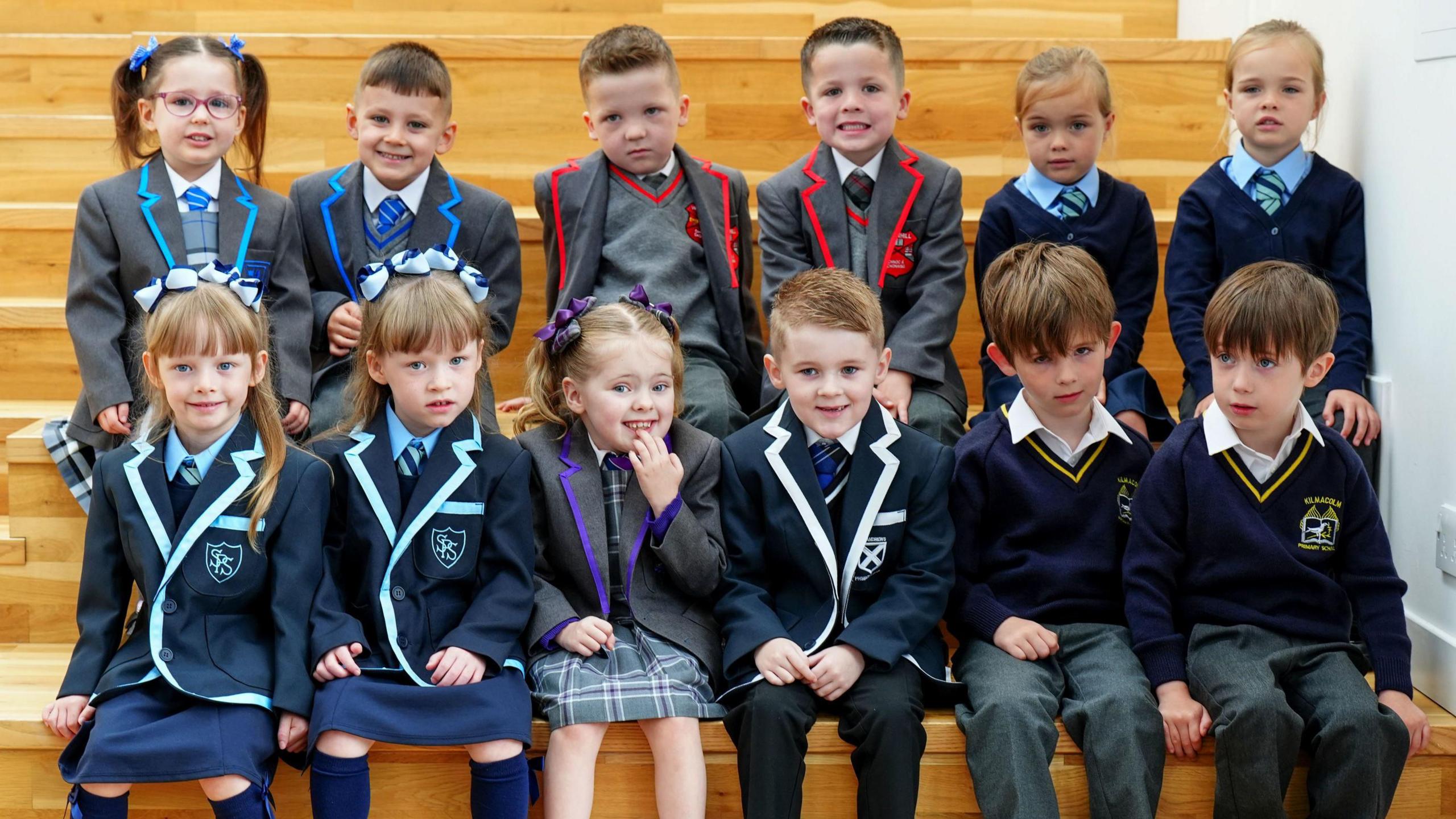 12 kids sit together in pairs in different sets of uniforms