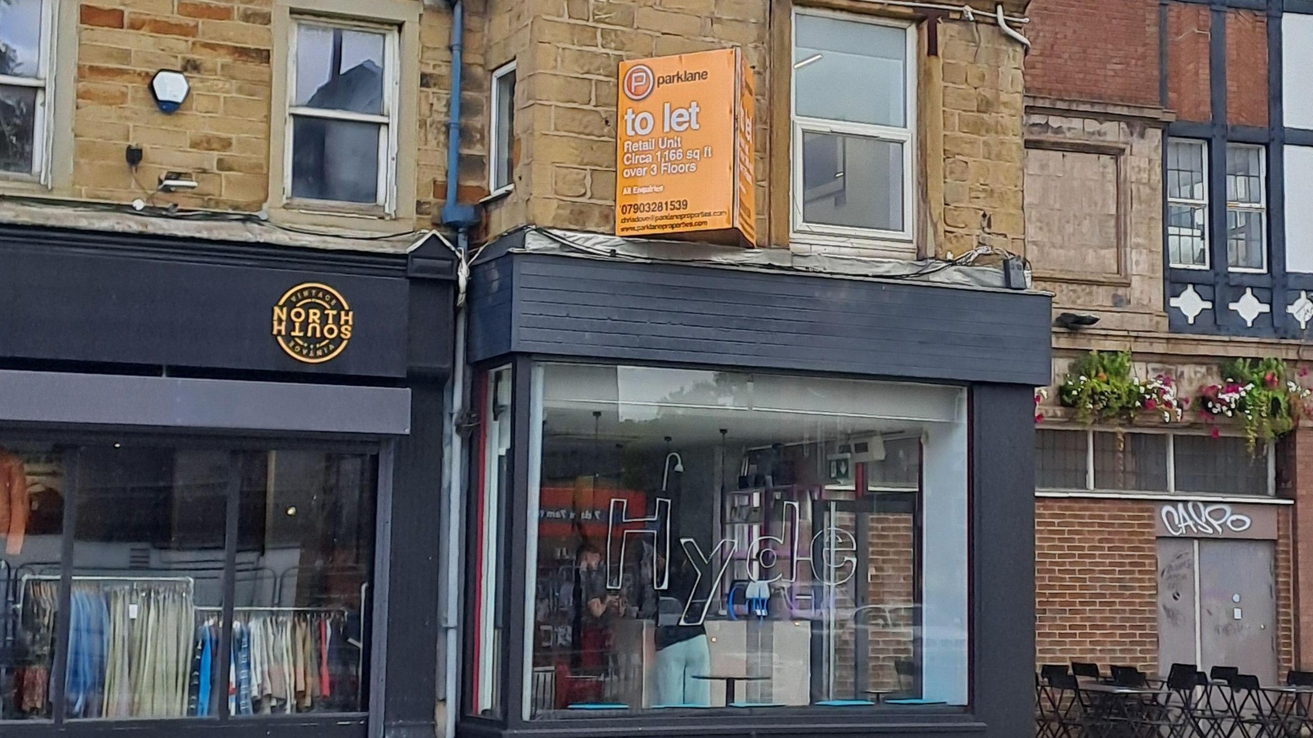 The glass front of a coffee shop. A clothes store, with clothes hanging in the window is nextdoor.