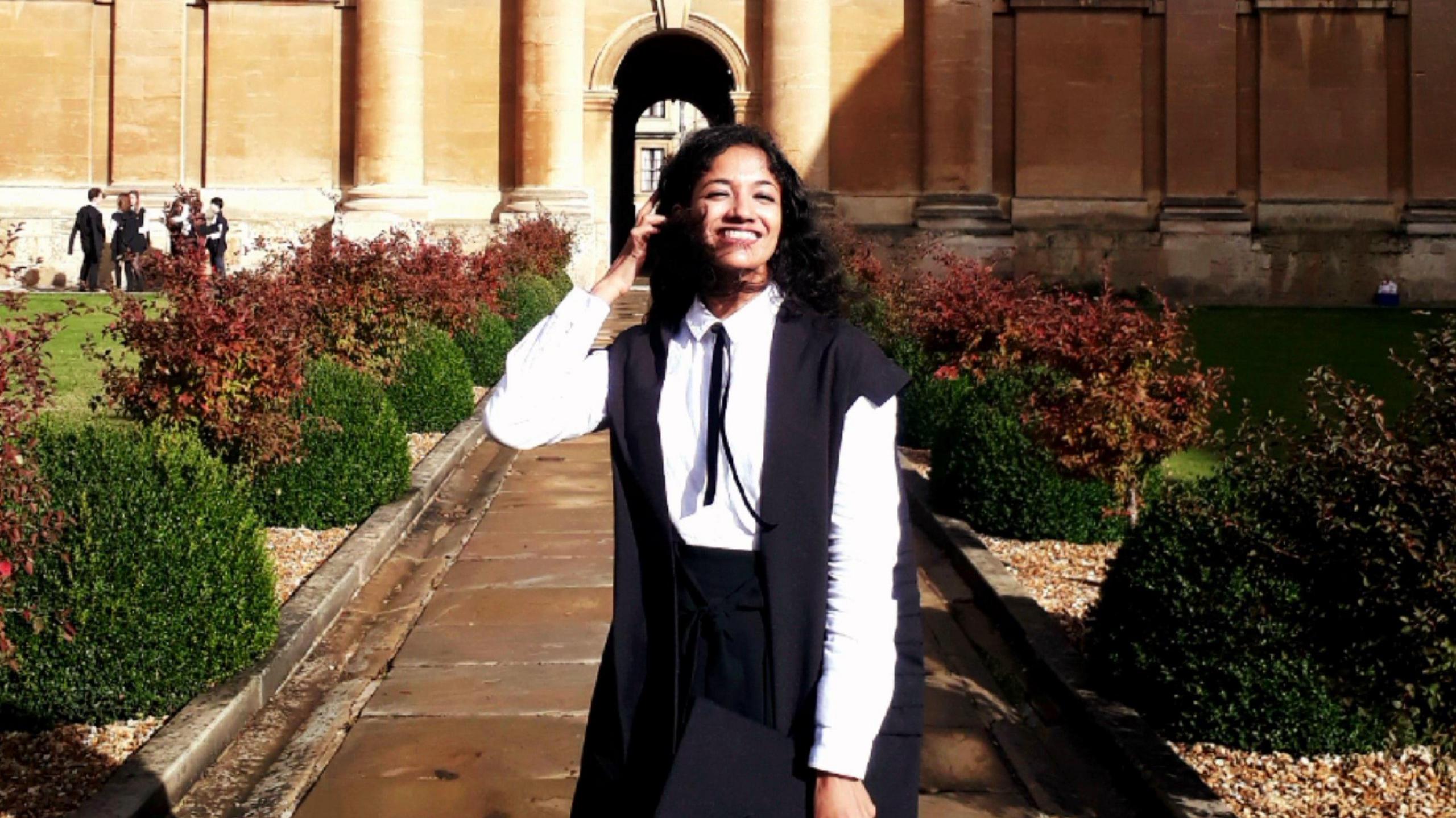 Lakshmi Balakrishnan stood black sub fusc gown in front of an oxford university building