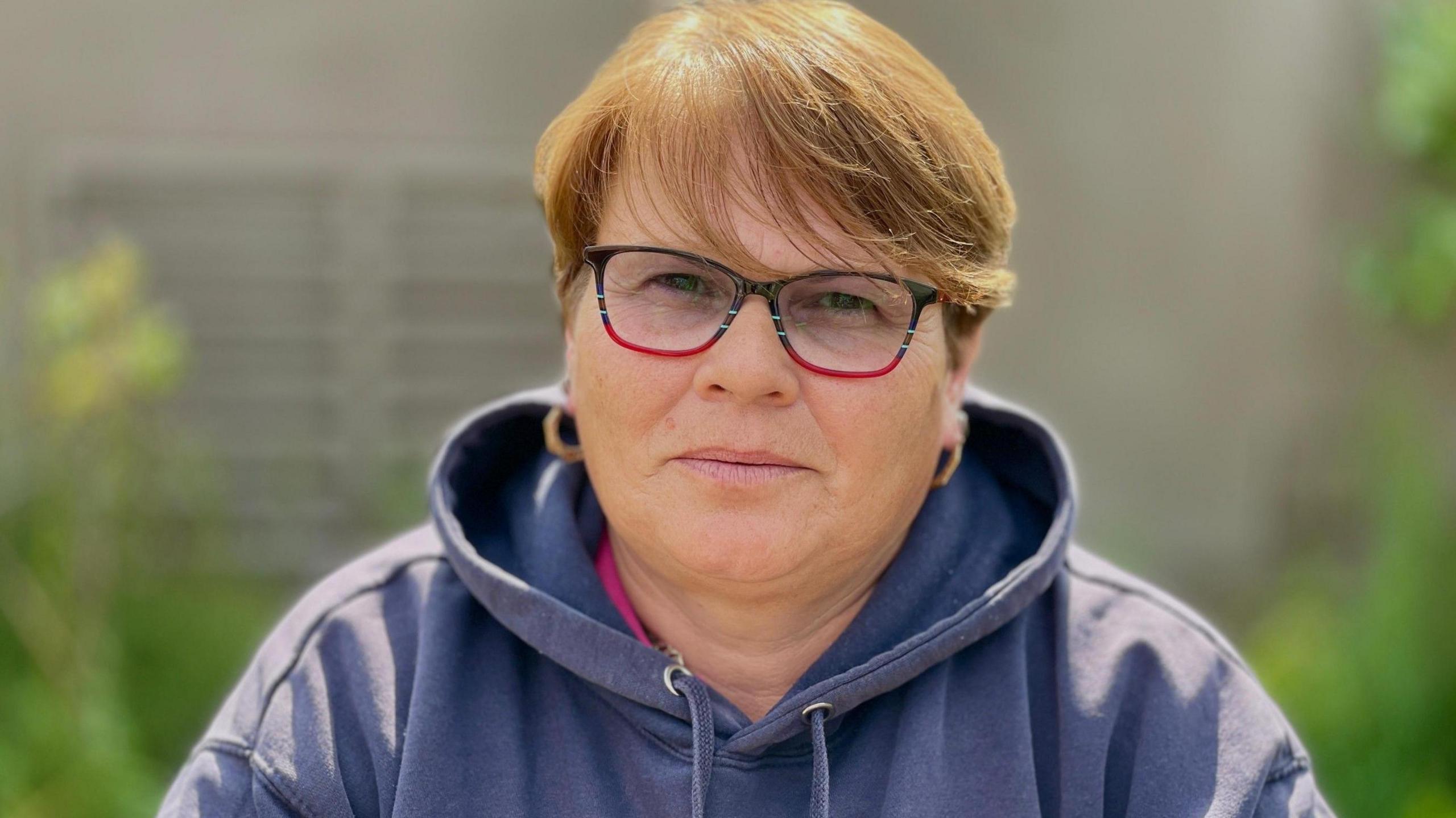 A woman in a light blue hoody and short red hair and glasses.