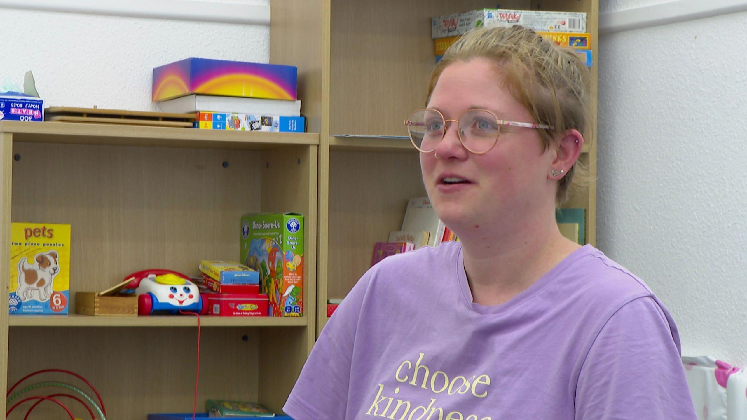 A woman sits in front of shelves full of toys.