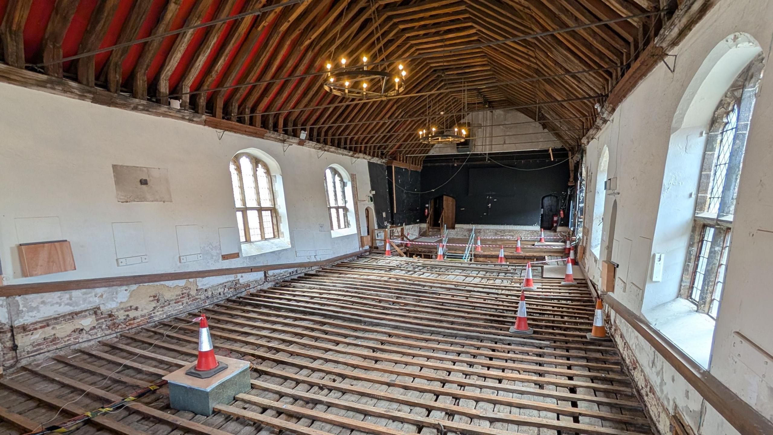 Inside the guildhall's roof. There are wooden beams over the floor and orange traffic cones on top of these. The roof is arched with lots of large wooden beams. 