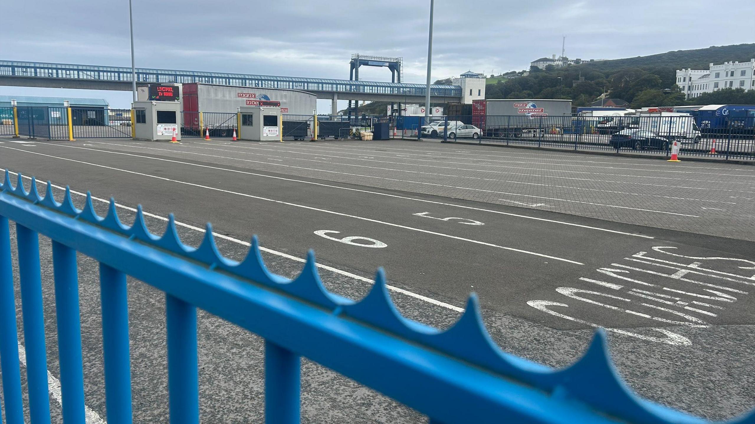 A large tarmacked area, with white painted lines to create numbered lanes for vehicles to park. It is empty and there is a blue railing in the foreground.