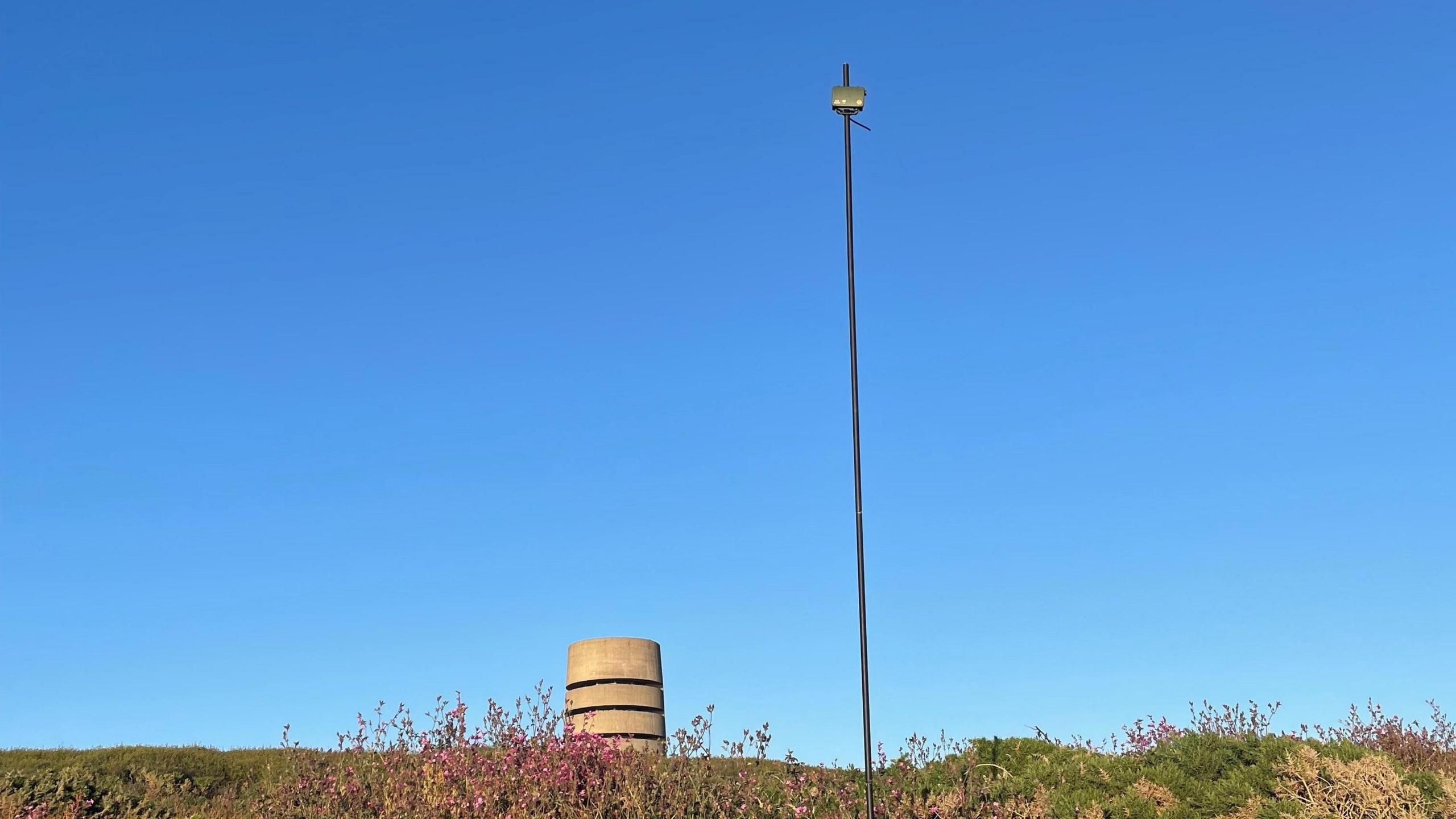 A bat detector on top of a long pole. A German world war two fortification is in the background