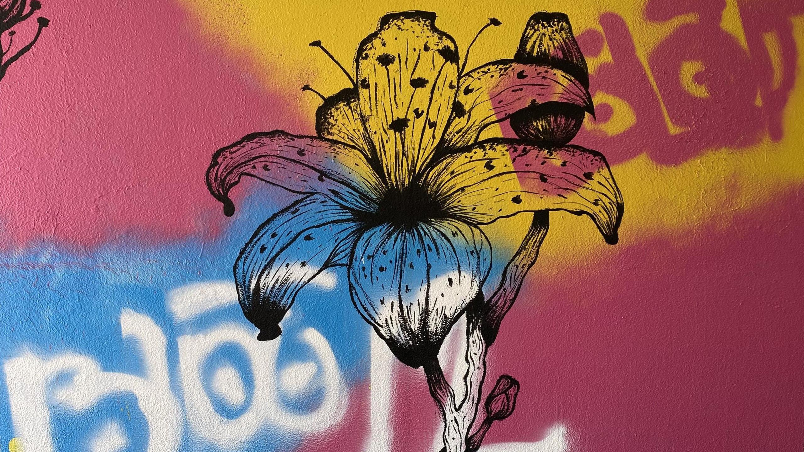 A large flower painted in black on a pink, yellow and blue subway wall.