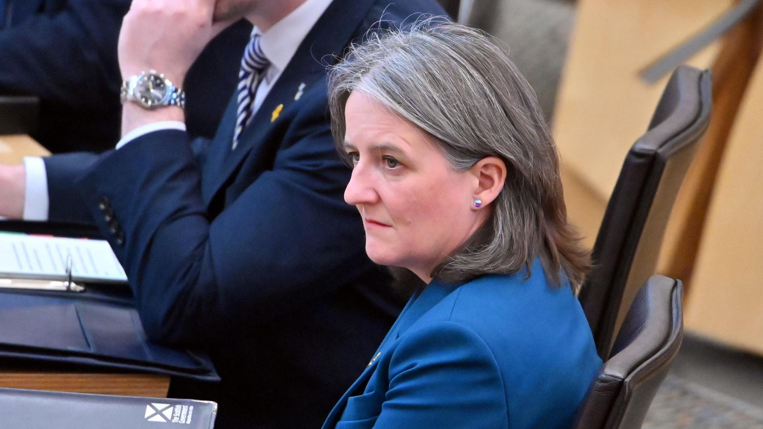 Scottish government social care minister Maree Todd sitting in Holyrood, side on to the camera and with a serious expression on her face