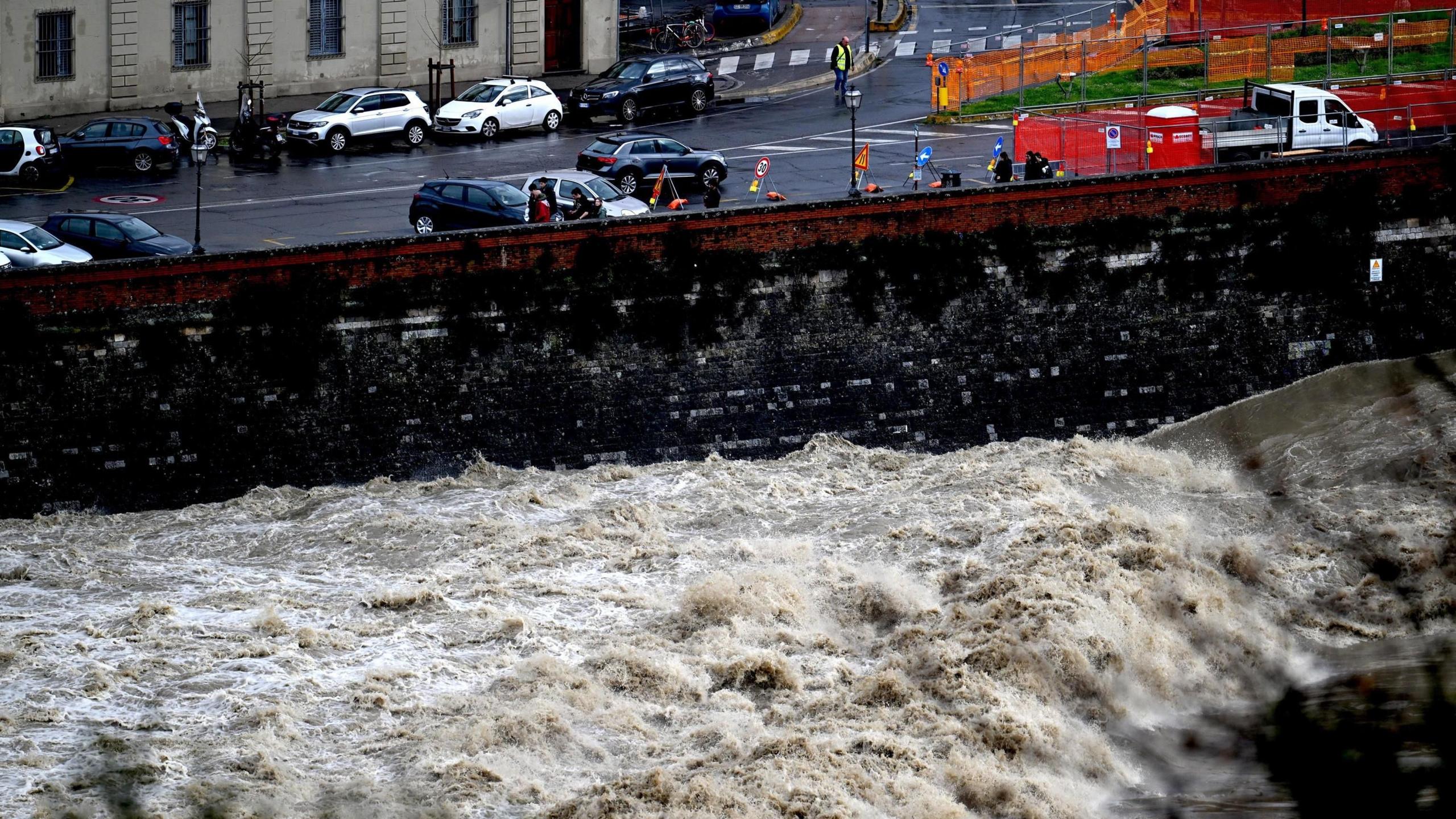 The swollen Arno river hits against a black wall beneath a road in Florence.