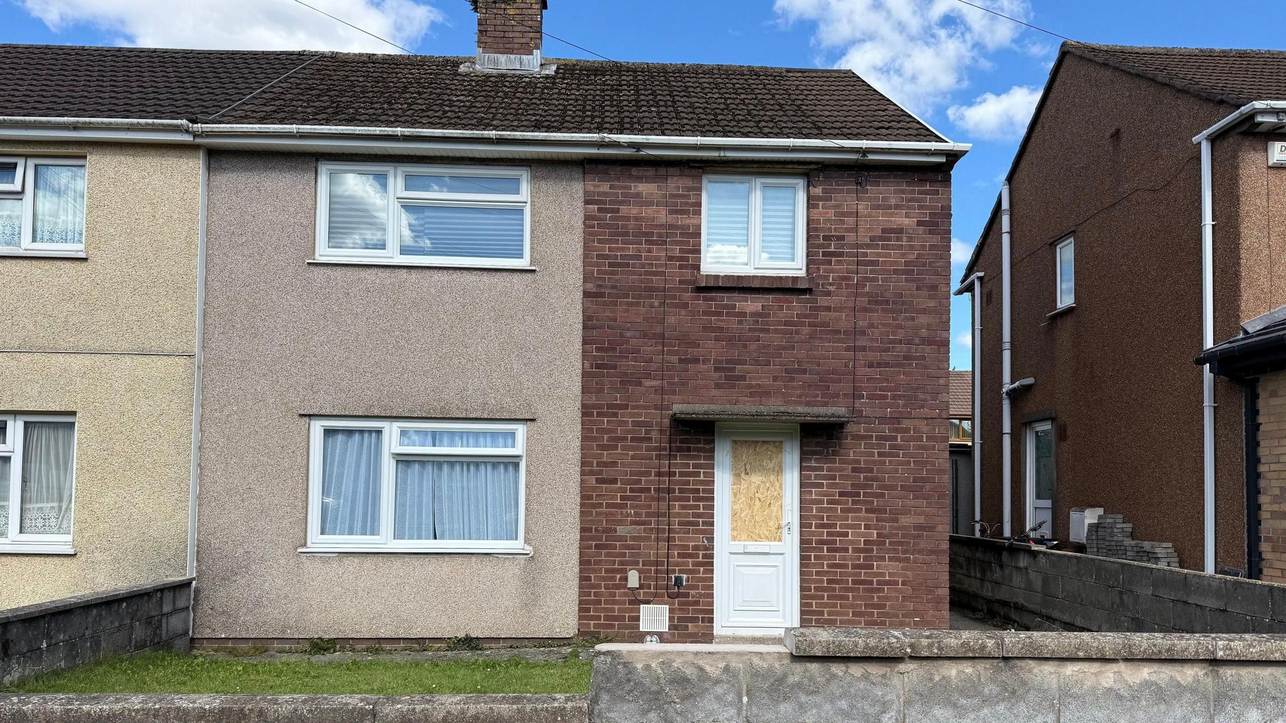 Image of the front of a house, with a board over the glass panel in the front door.