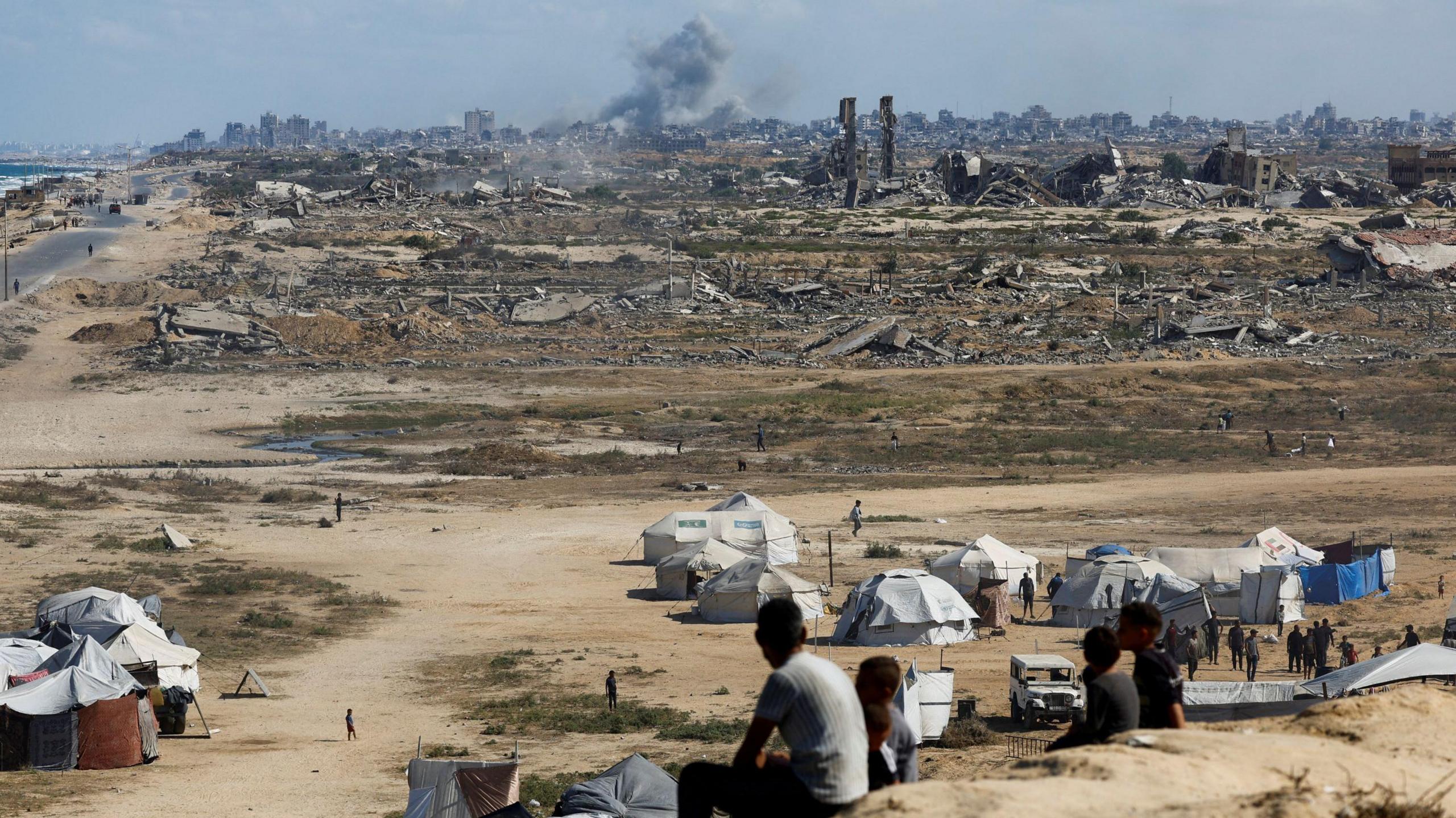 Palestinians look on as smoke rises following explosions in Gaza City, as seen from central Gaza Strip October 5, 2025