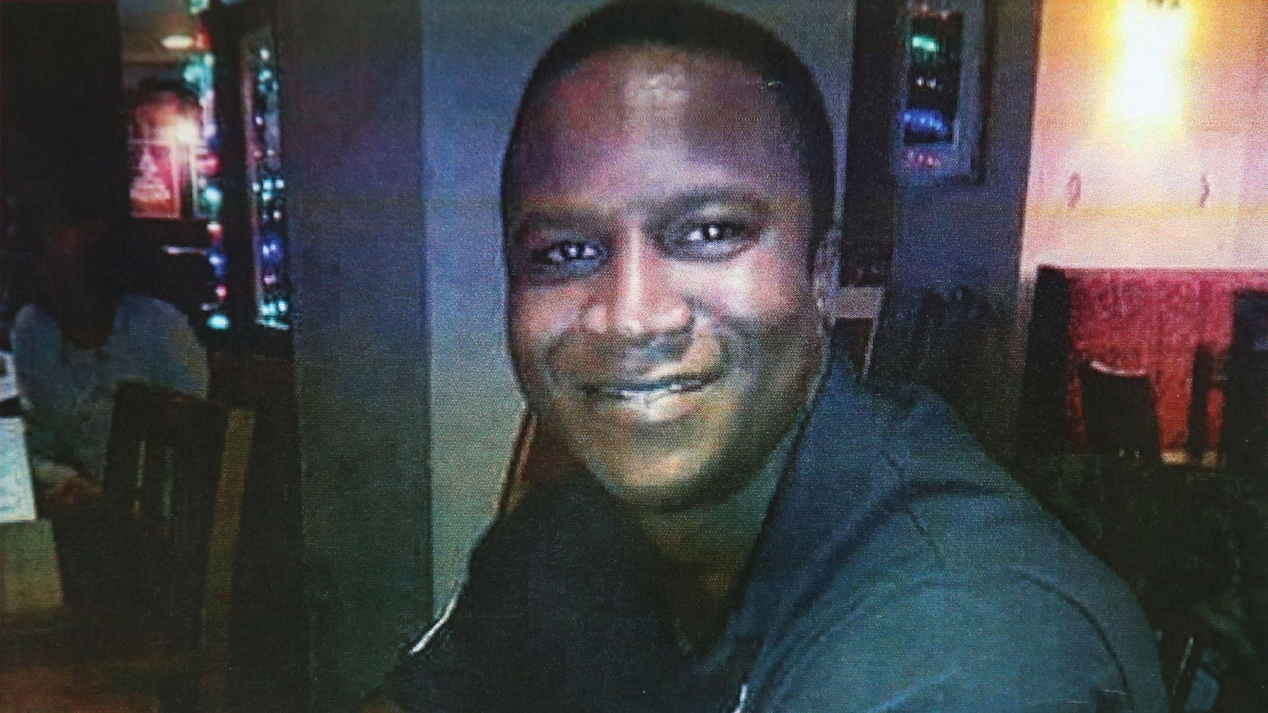 Sheku Bayoh smiles for a photograph in what appears to be a café or pub setting.   