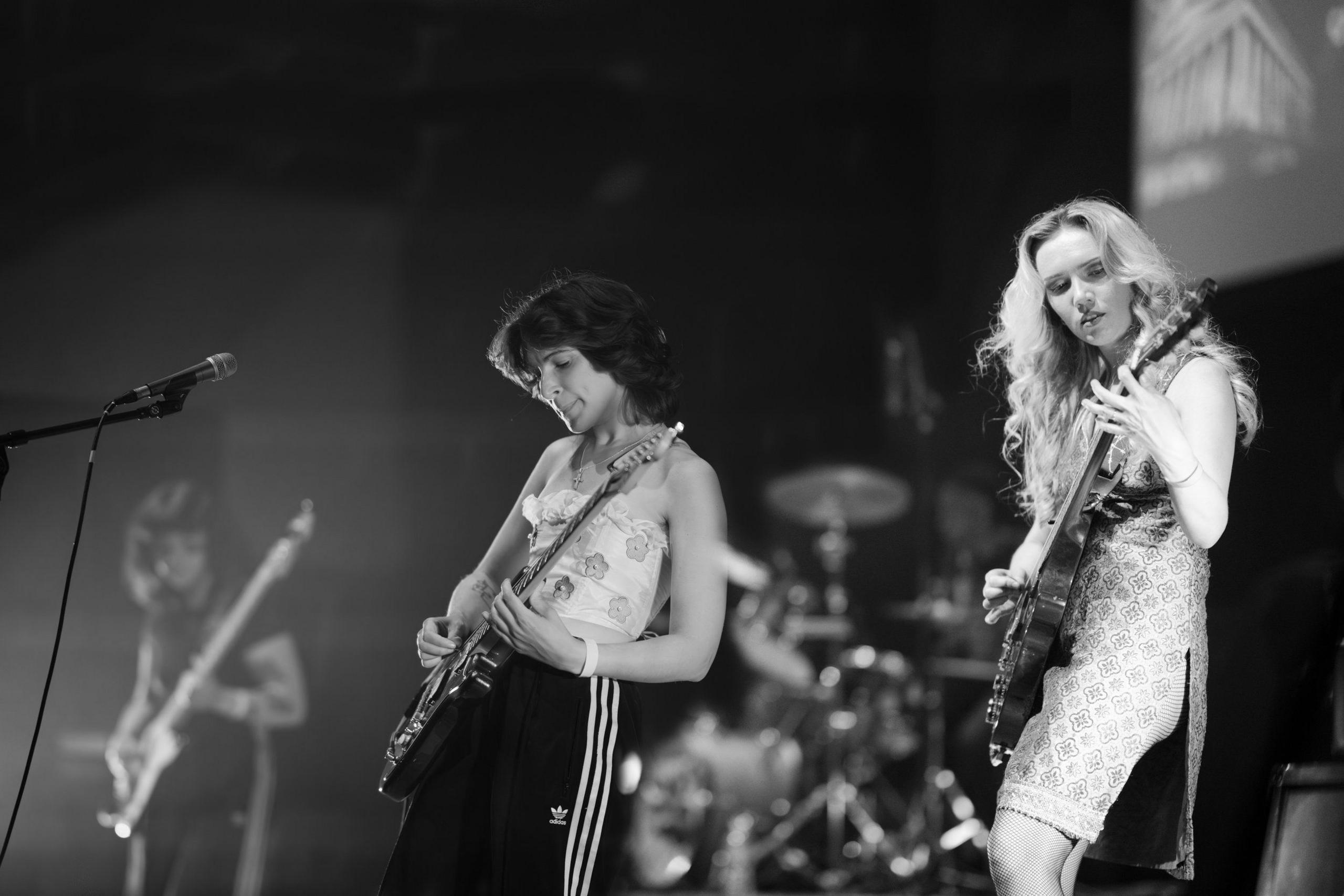 Two female members of Meatdripper are seen on stage in a black and white image. They both have guitars.