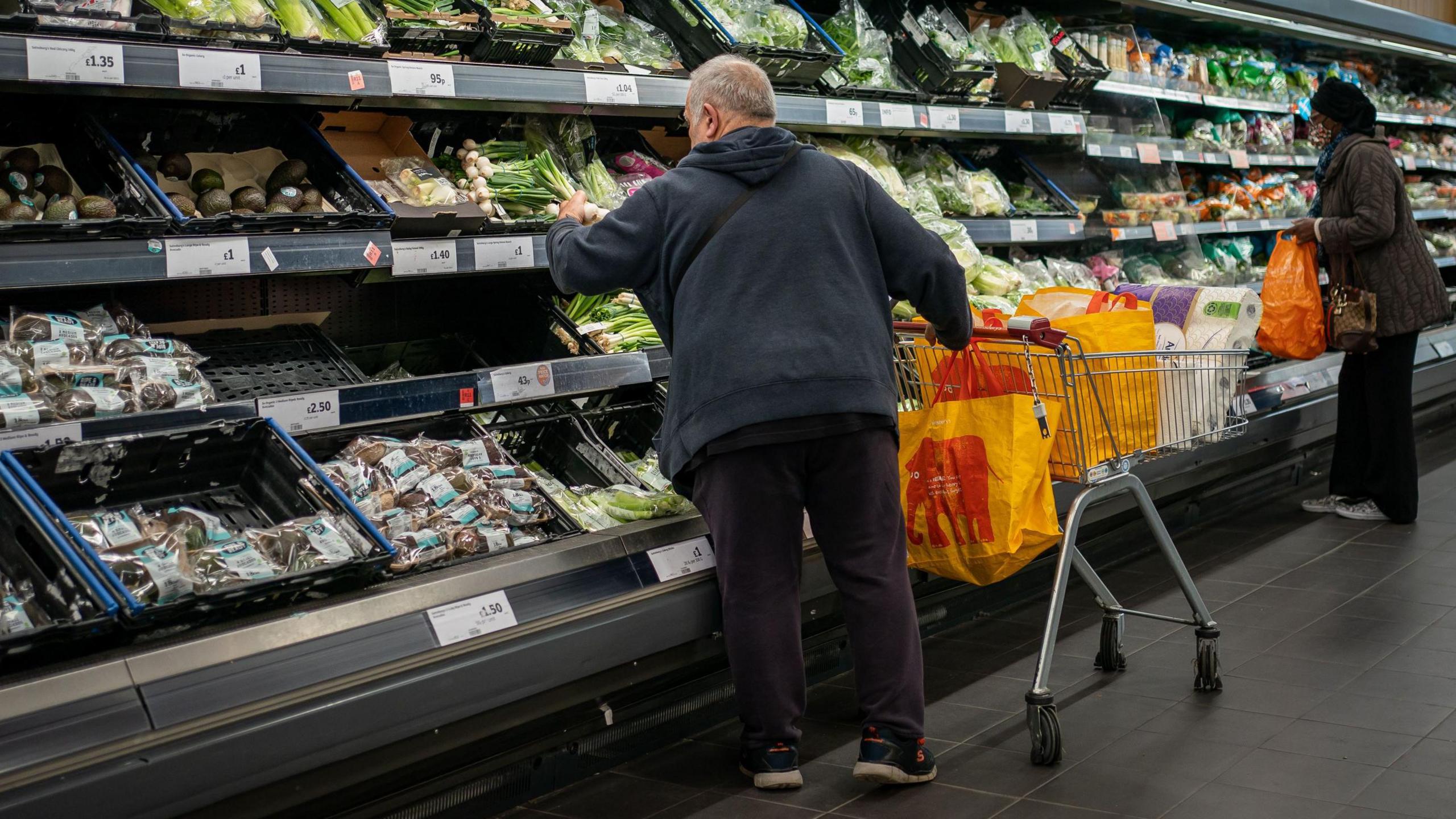 Man in dark hoodie with trolley shops in fruit and vegetable section at Sainsbury's