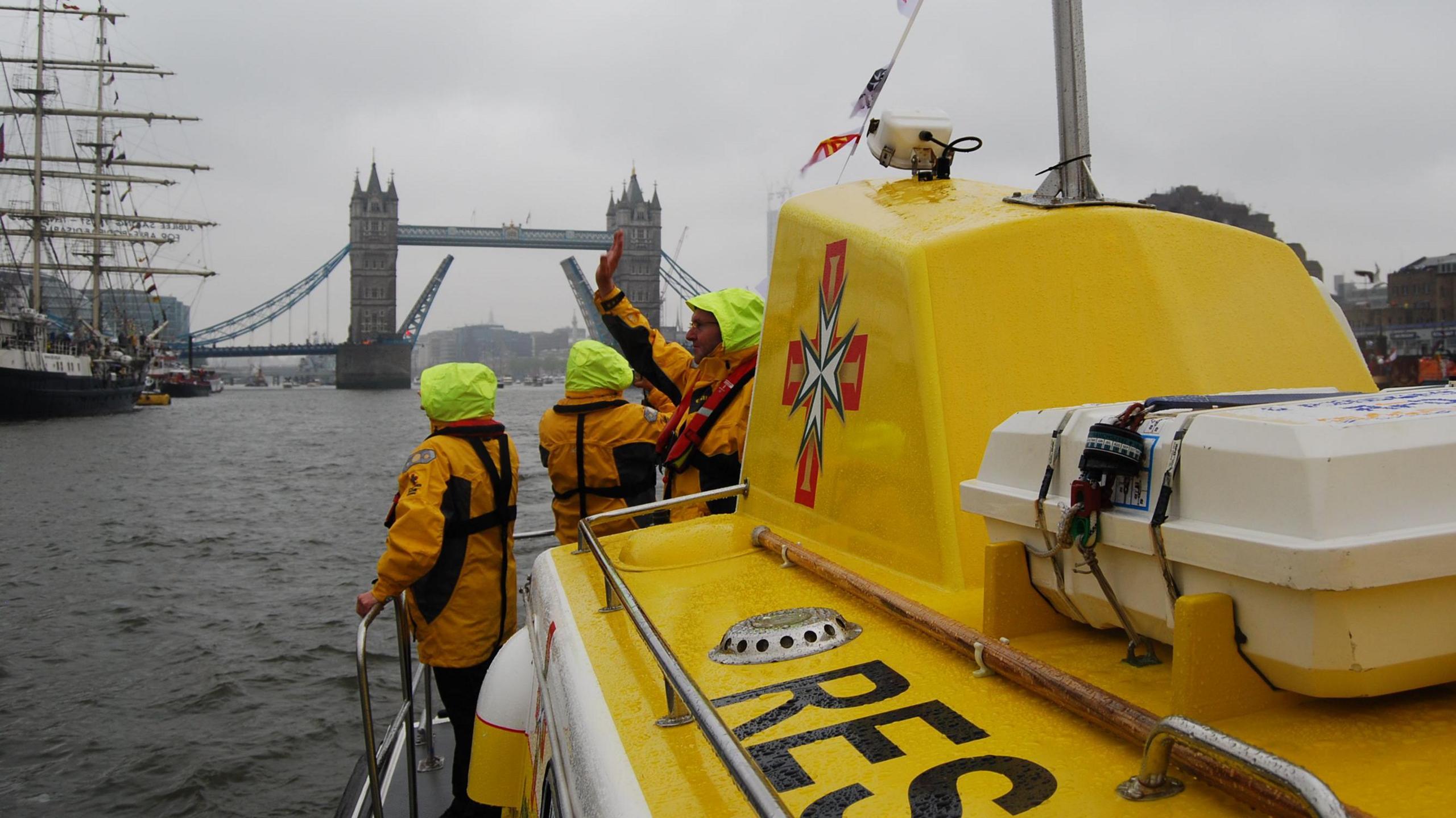 People stood on bow of marine ambulance as it travels on the Thames with Tower Bridge in the background