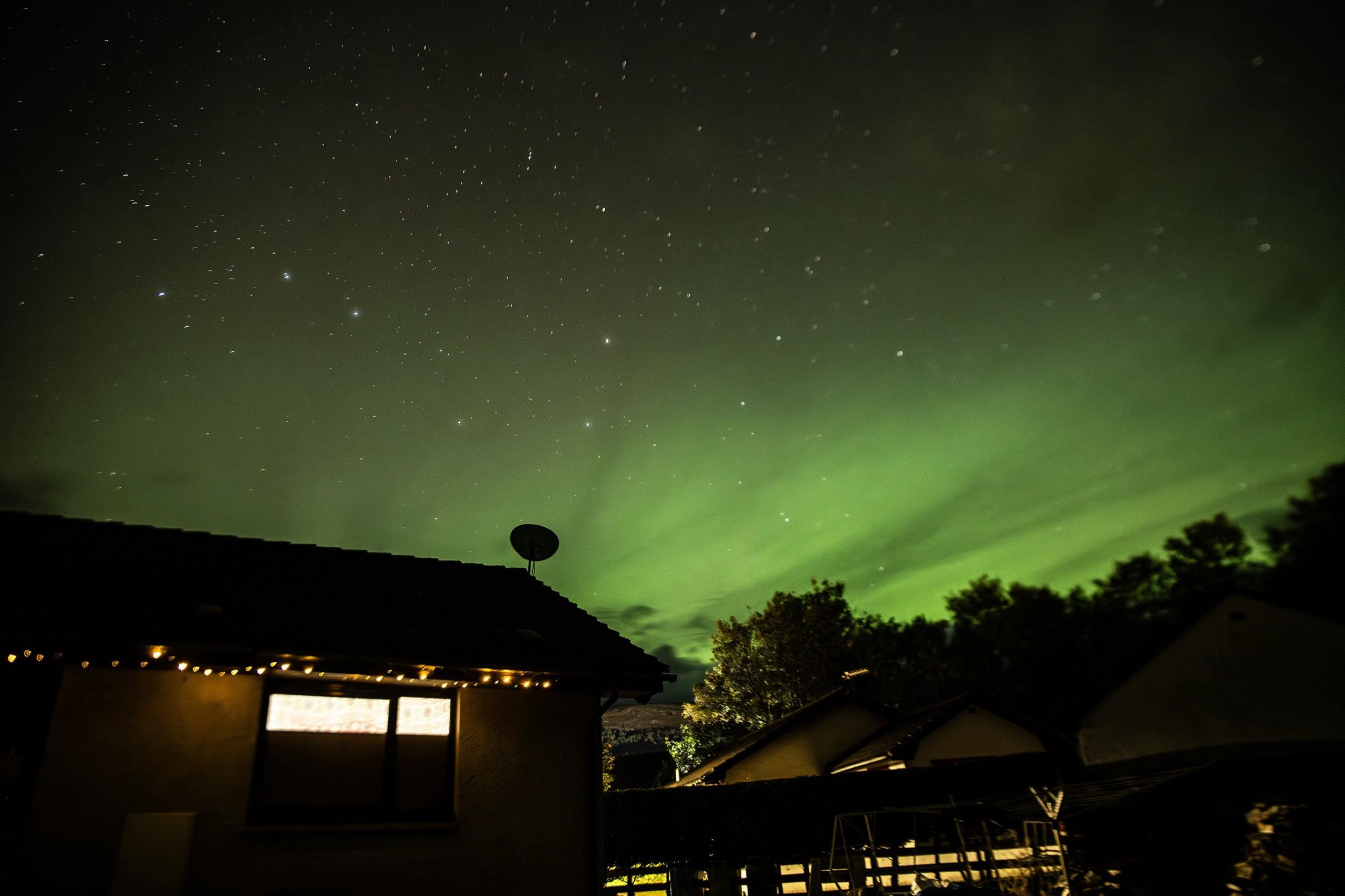 A green tinted aurora filling a starry sky above a house at night