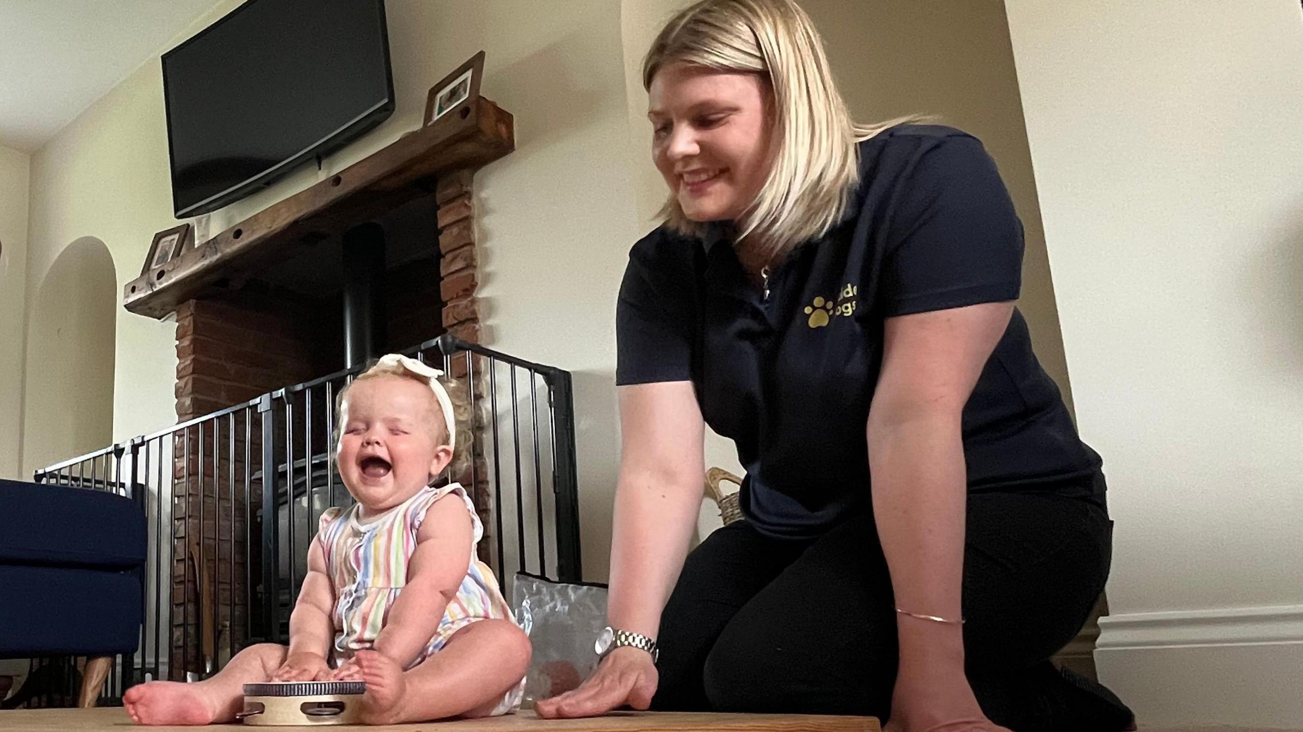 Margot pictured laughing, holding a tamborine, pictured alongside Kate Reed, a therapy worker from Guide Dogs